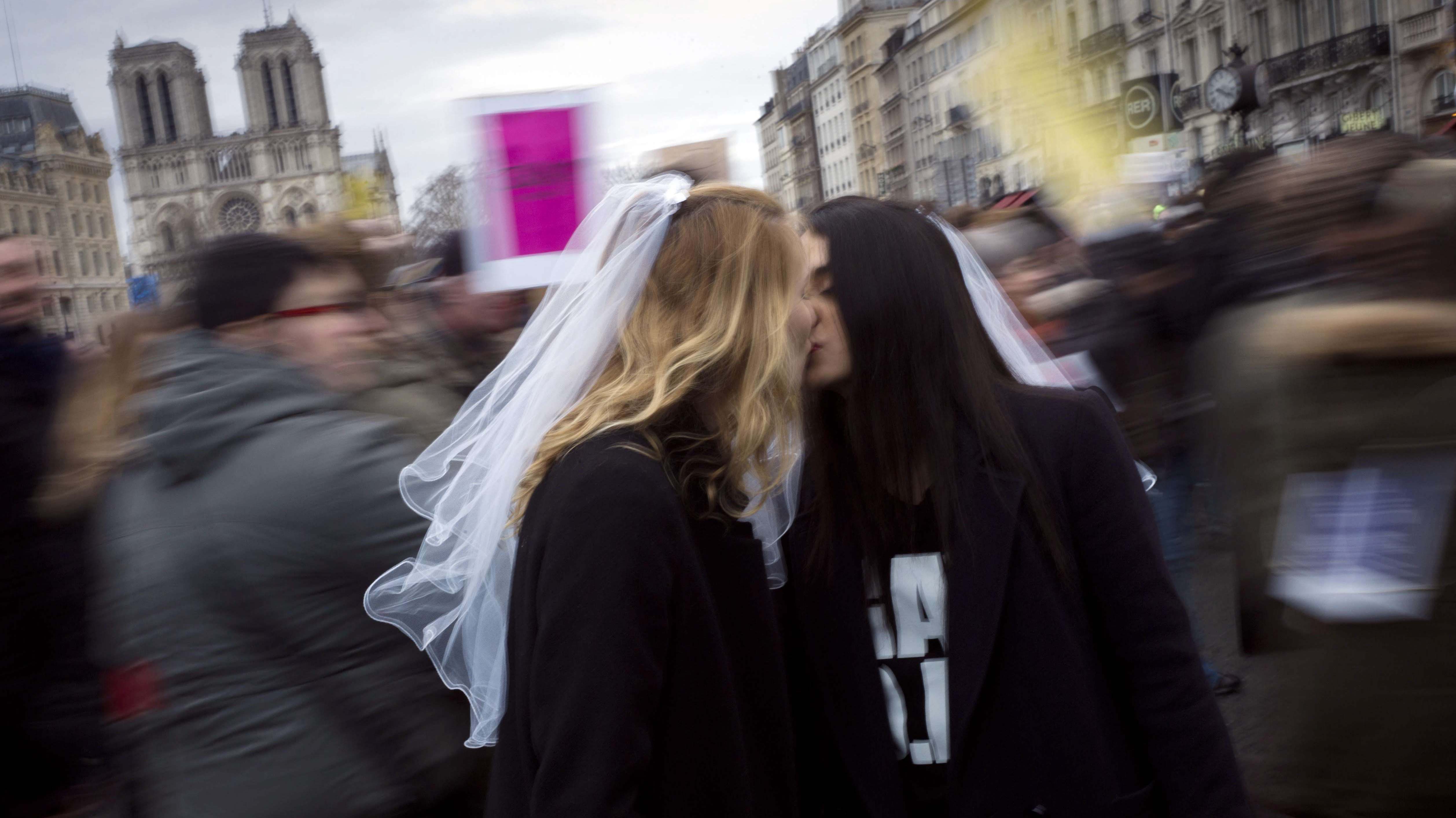 Zwei Frauen mit Brautschleiern küssen sich in Paris.