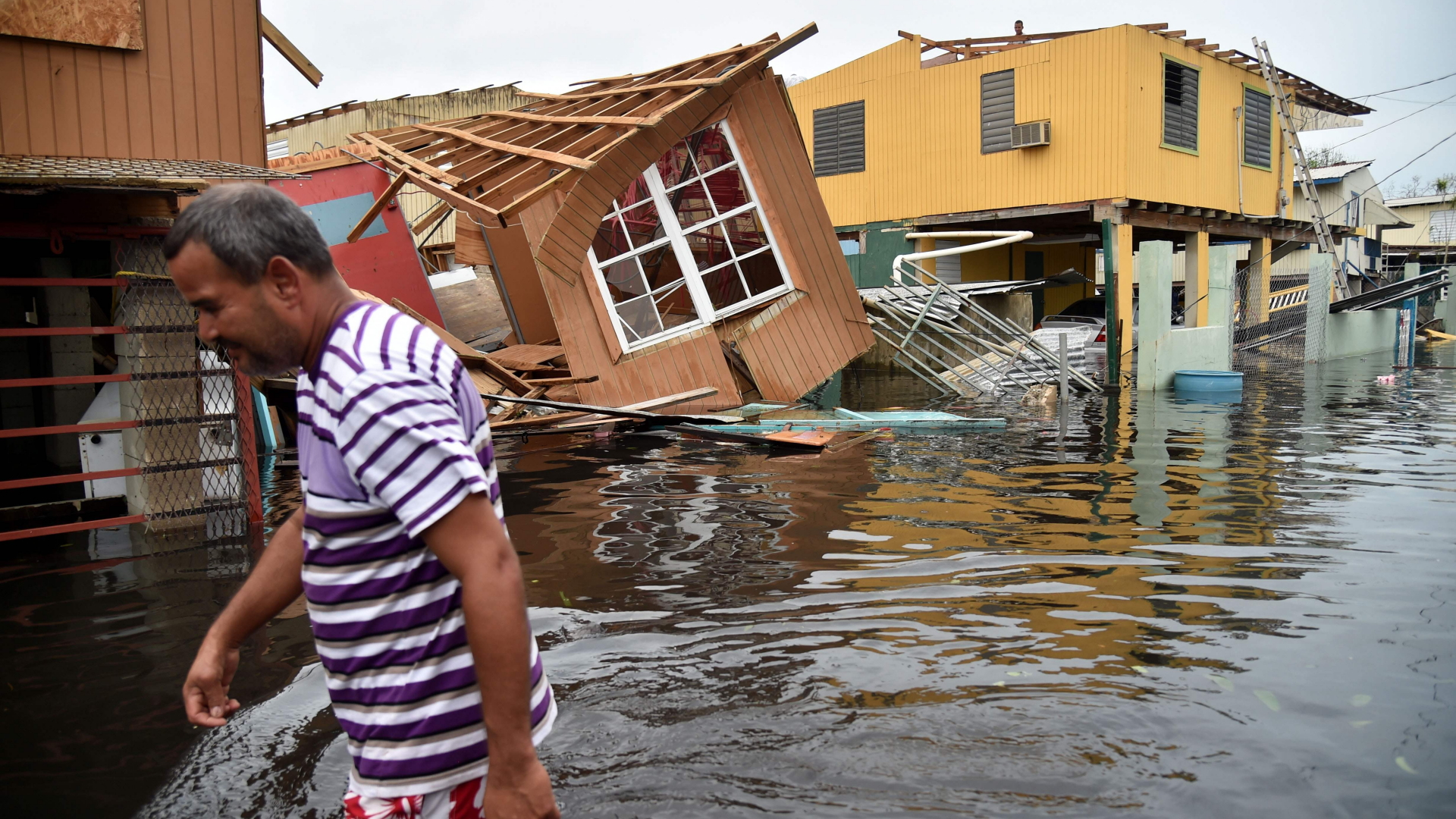 Ein Mann watet auf einer überfluteten Straße an völlig zerstörten Häusern auf der Karibikinsel Puerto Rico vorbei. | AFP