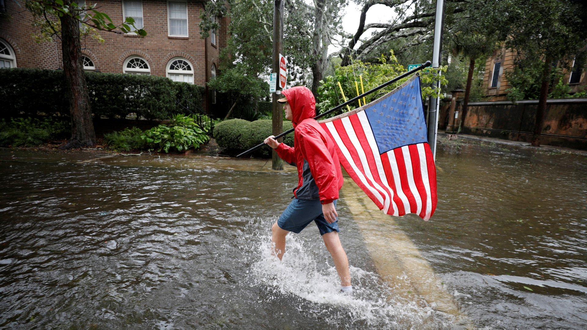 Ein Mann mit einer amerikanischen Flagge läuft durch eine überflutete Straße im US-Bundesstaat South Carolina. | REUTERS