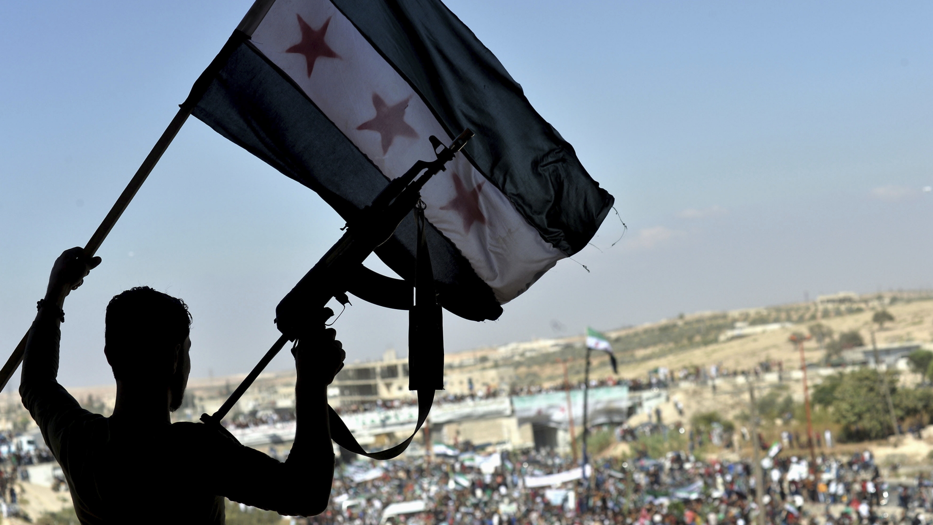 Ein Demonstrant schwenkt eine syrische Fahne und hält ein Gewehr hoch bei einem Protest gegen die Offensive der syrischen Regierung in der Provinz Idlib. | Bildquelle: dpa