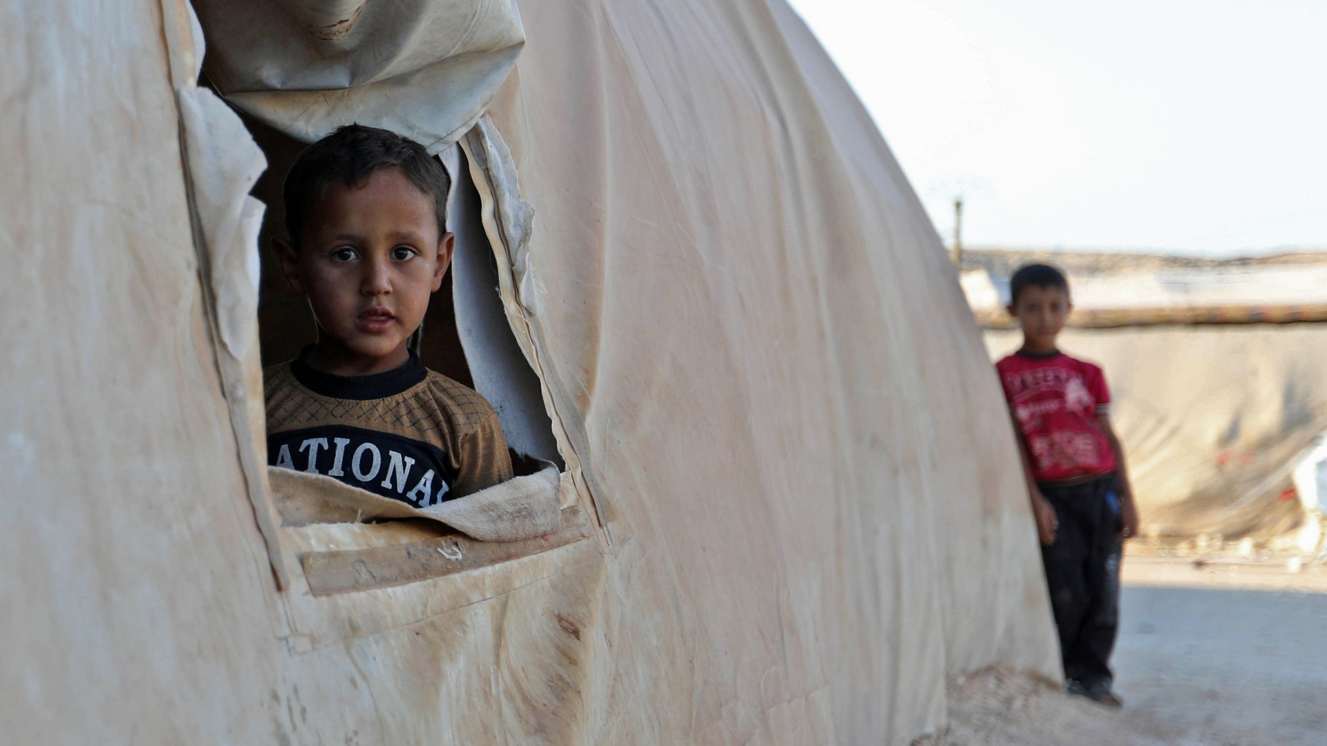Ein Kind schaut in einem Flüchtlingslager in der syrischen Provinz Idlib aus einem Zelt. | AFP