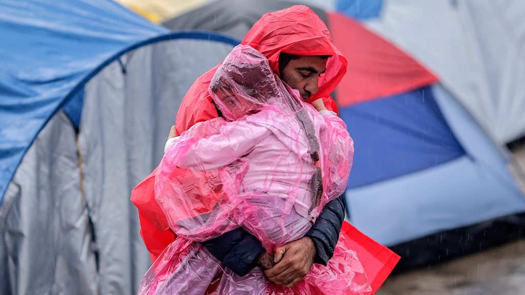 Ein Mann in Plastikcape trägt ein Kind durch zahlreiche Zelte