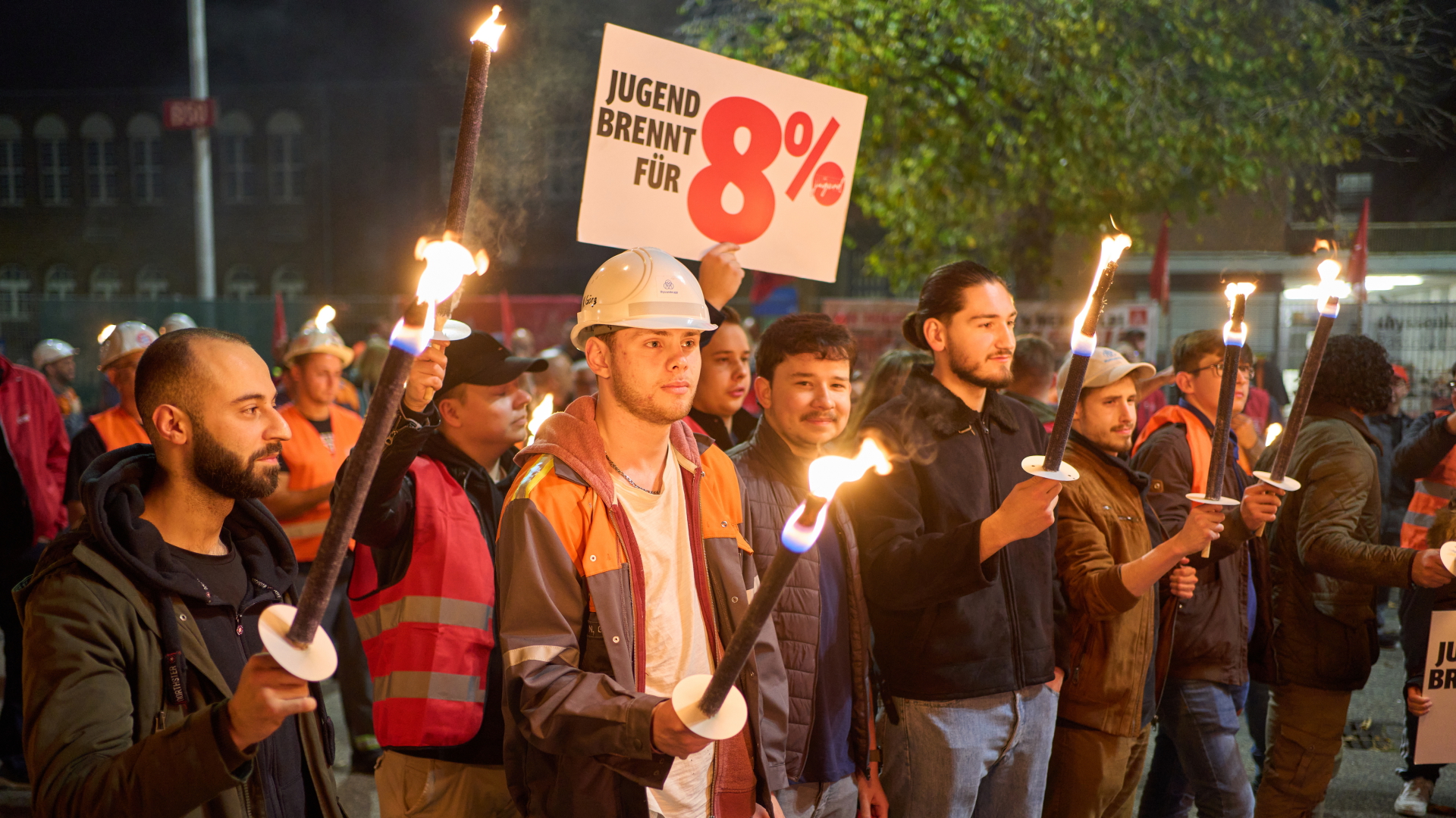 Beschäftigte eines Unternehmens in Andernach nehmen mit Fackeln und einem 8-Prozent-Schild an einem Warnstreik teil. | dpa