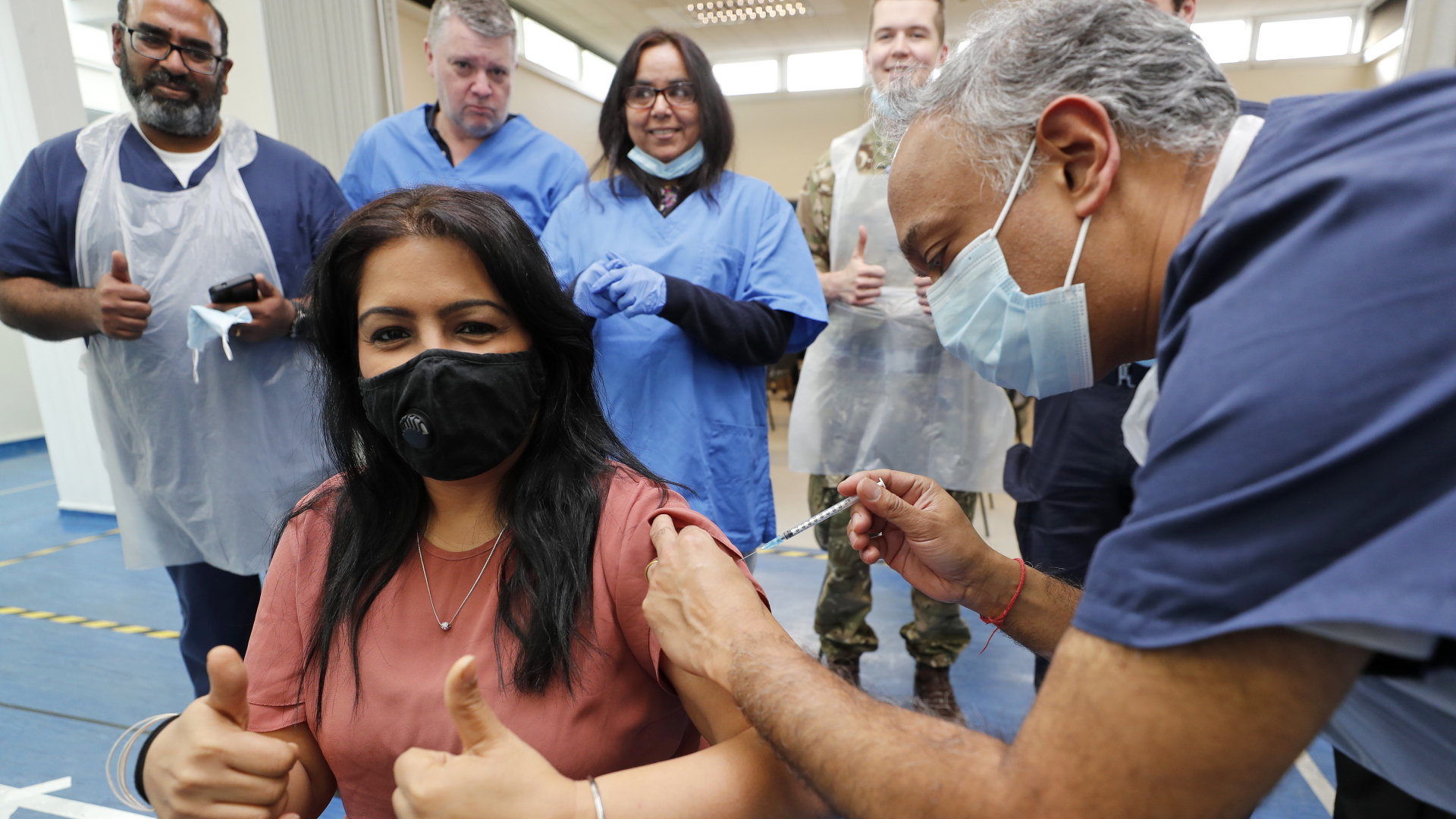 Der Arzt Anil Mehta verabreicht, umgeben von seinem Team aus Doktoren und Arzthelfern, Geeta Waddon ihre Corona-Schutzimpfung - und dabei die 10.000ste Impfung in seiner Praxis. | dpa
