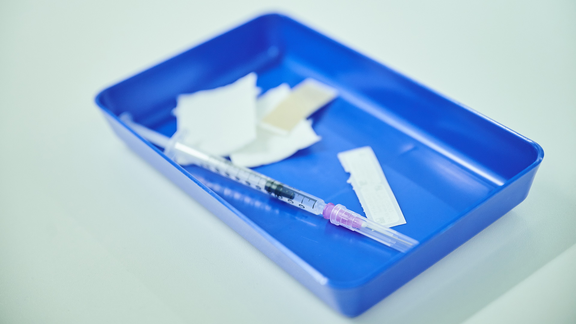 Eine aufgezogene Spritze mit Impfstoff liegt in einer blauen Schale. | dpa