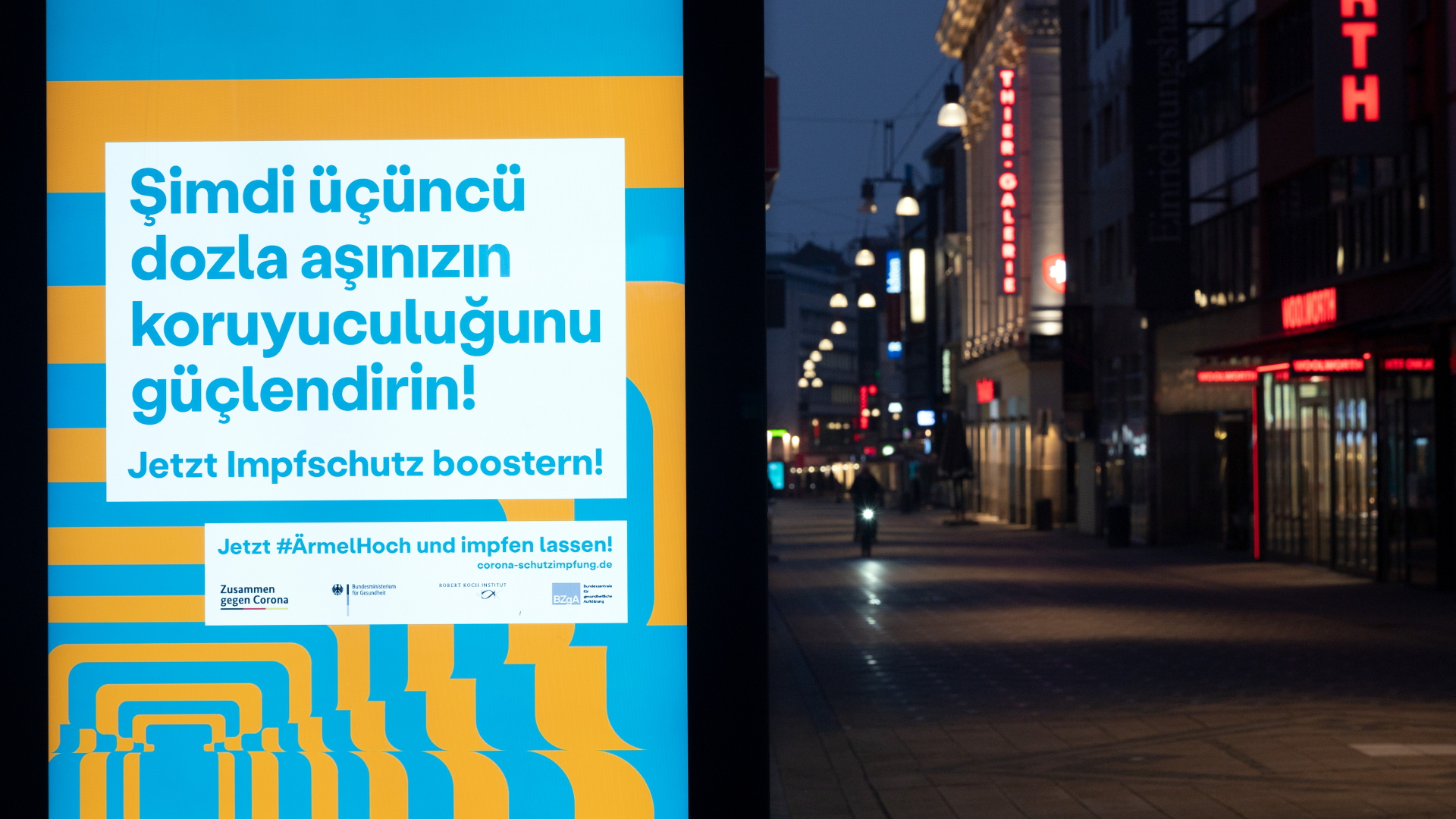 "Jetzt Impfschutz boostern!" ist auch in türkischer Sprache auf einem Werbedisplay in einer Fußgängerzone zu lesen. | dpa