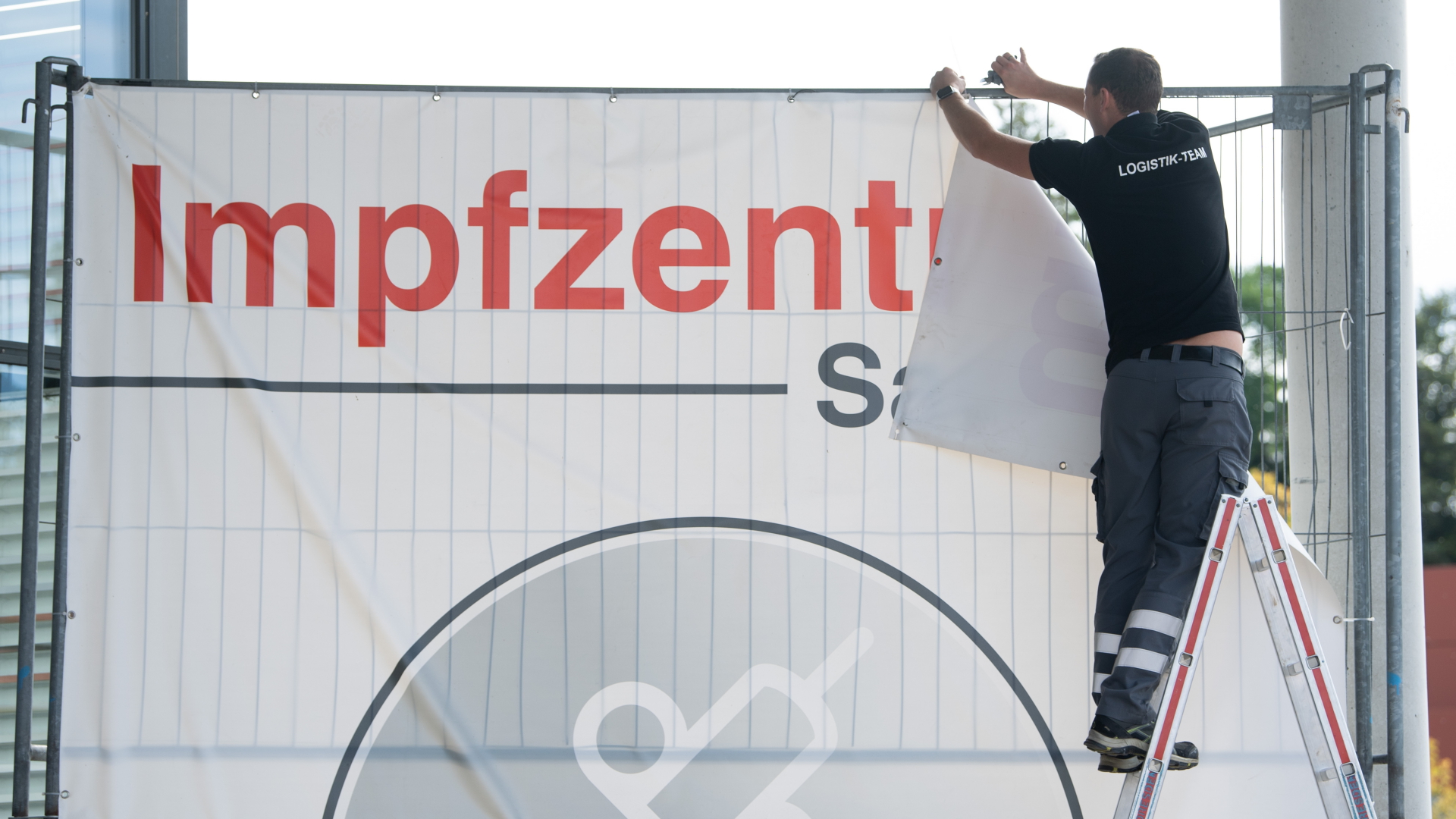 Ein Banner mit der Aufschrift "Impfzentrum Sachsen" wird von einem Bauzaun entfernt