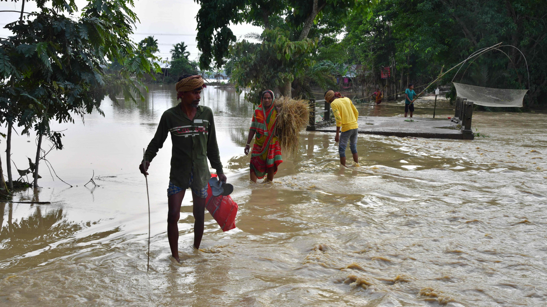 Dorfbewohner waten nach heftigen Regenfällen im indischen Bundesstaat Assam durch Hochwasser. | AFP