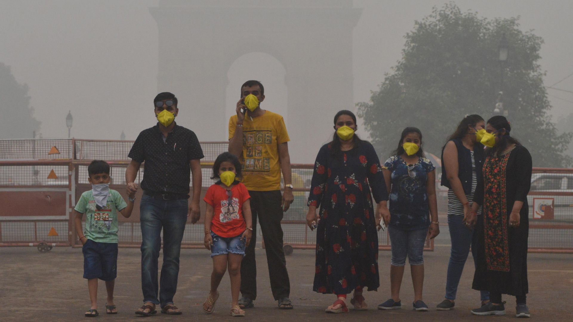 Menschen mit gelber Atemmaske stehen Anfang November 2019 in Neu Delhi. Im Hintergrund ist das India Gate in Smog eingehüllt. | dpa