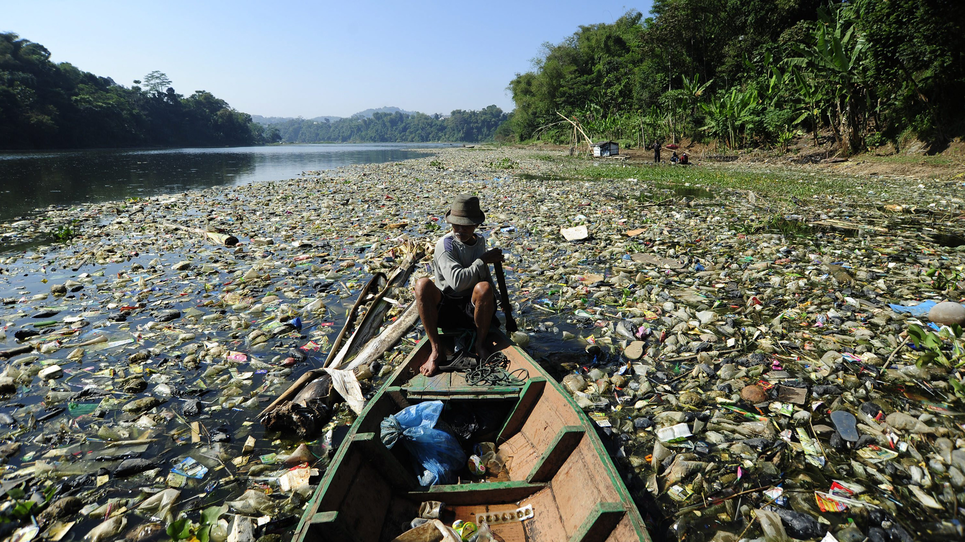 Ein Mann rudert im Boot auf dem mit Plastikmüll verschmutzten Citarum in Indonesien. | picture alliance / Xinhua News A