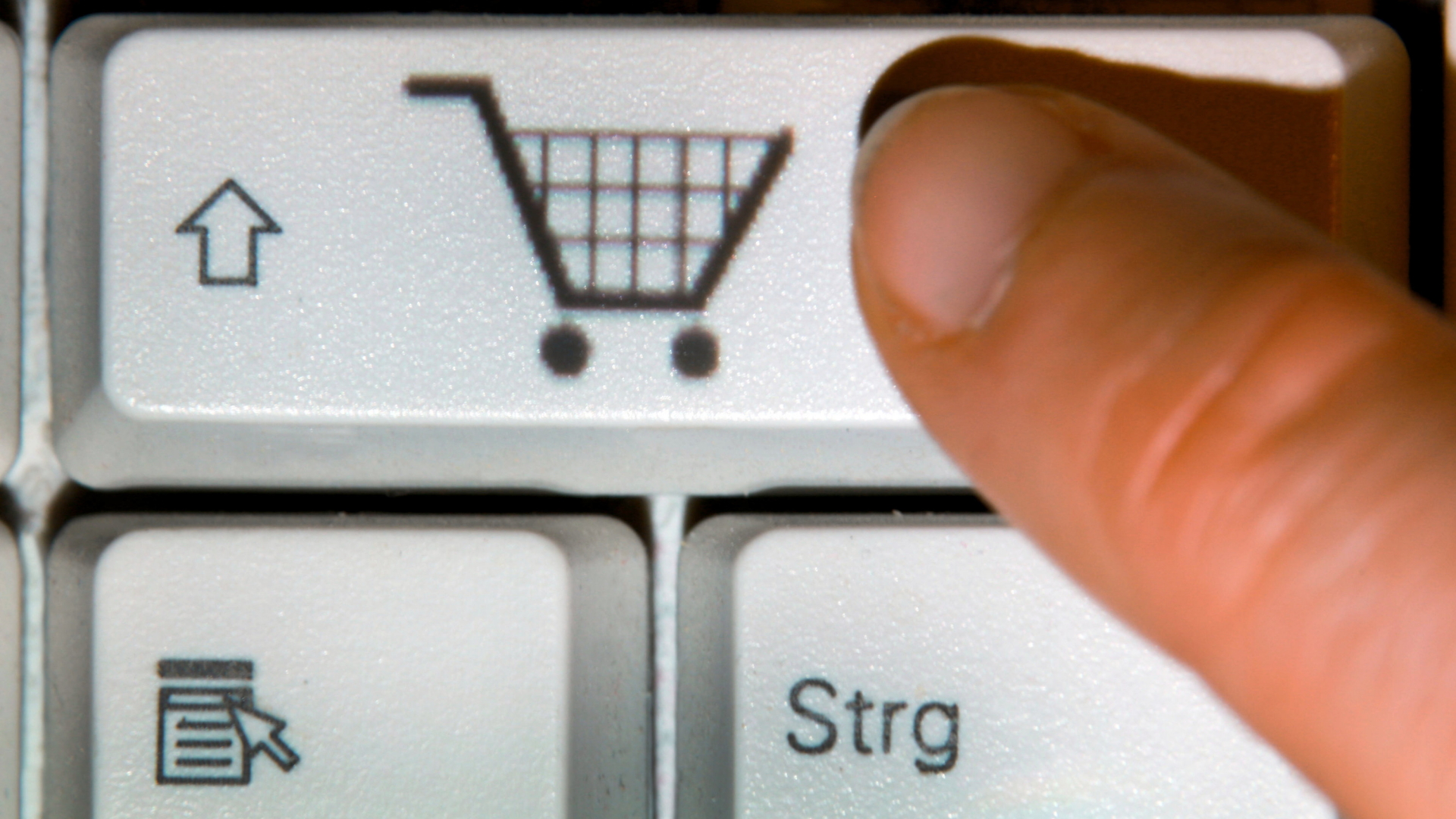 Ein Finger drückt auf einer Tastatur eine Taste mit dem Symbol eines Einkaufwagens.