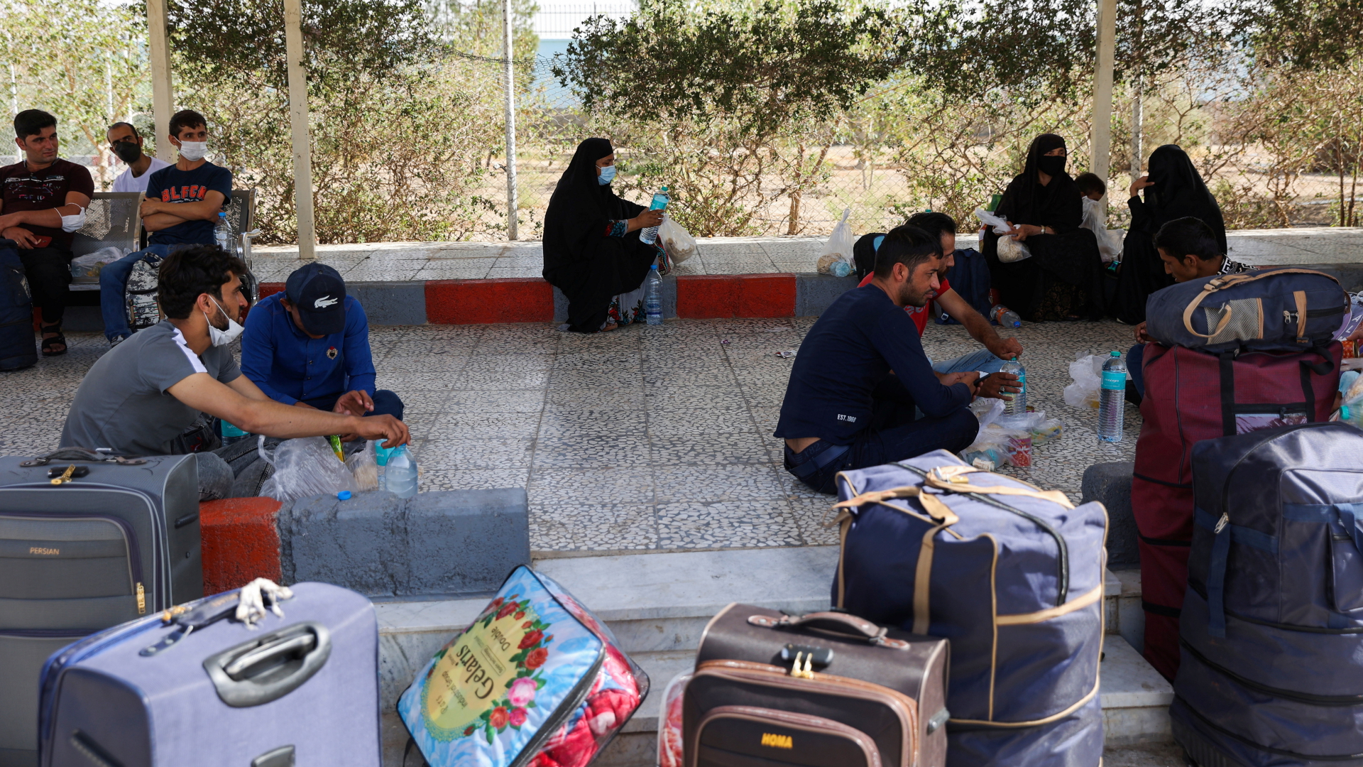 Geflohene Afghanen sitzen in einem Flüchtlingslager im Iran vor Gepäckstücken. | via REUTERS
