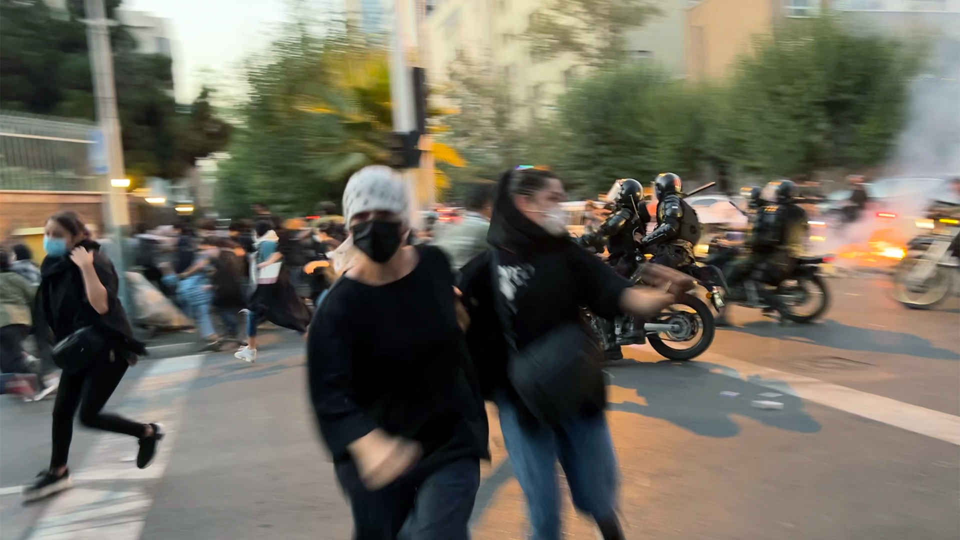 Zwei Frauen laufen auf der Straße, im Hintergrund fahren Polizisten auf Motorrädern