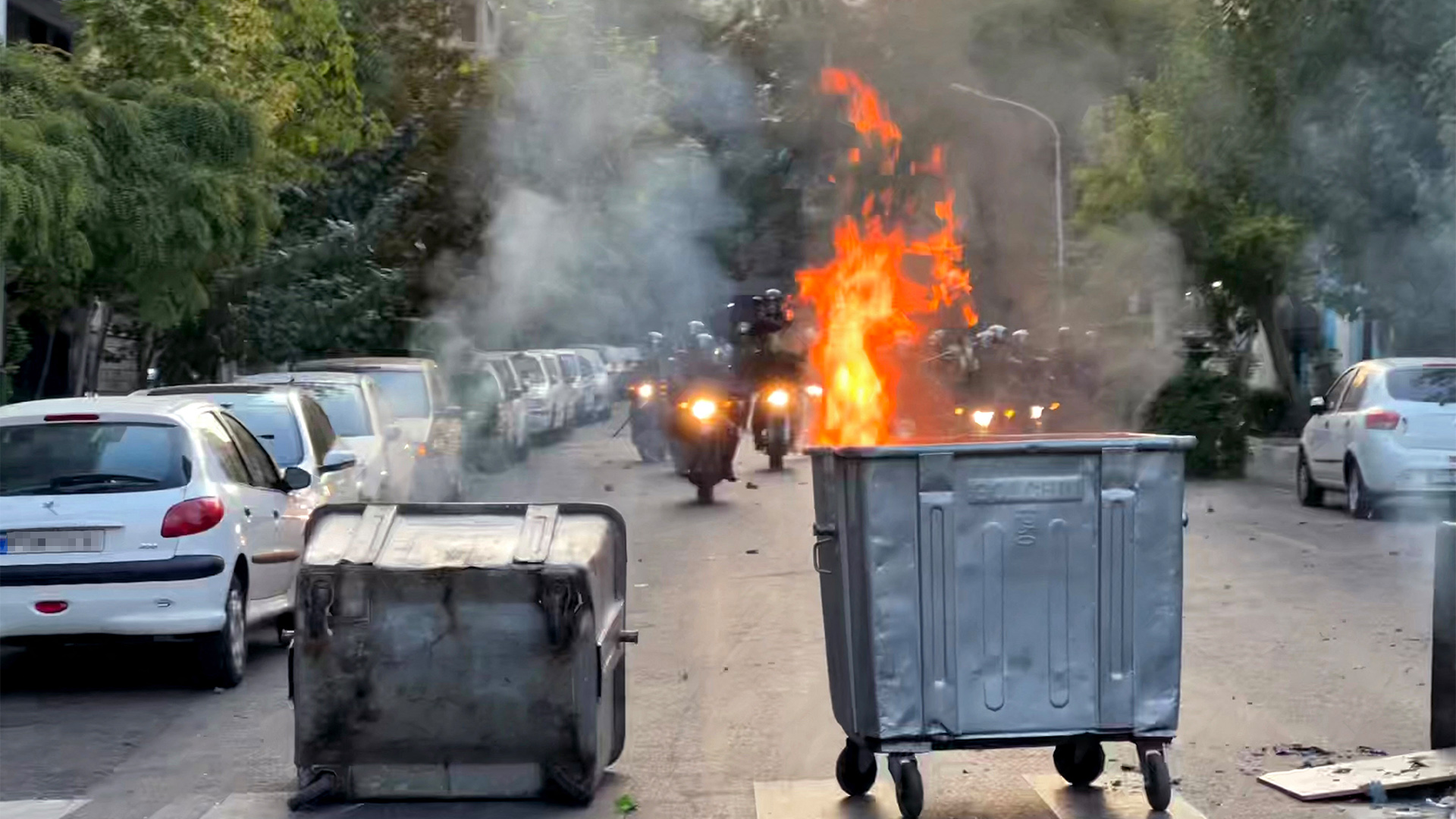 Bei Protesten im Iran fahren Polizeiwagen auf brennende Mülltonnen zu. | AFP