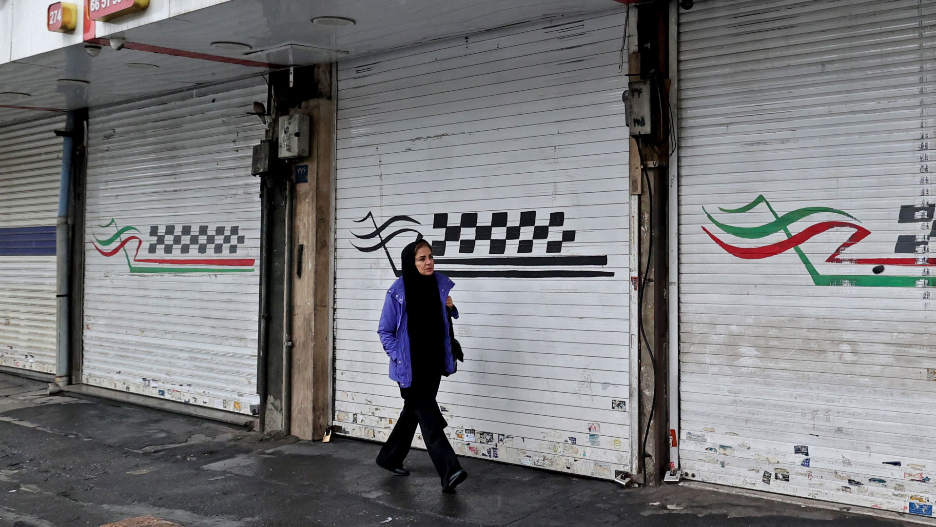 Eine Frau läuft vor einem geschlossenen Laden mit heruntergelassenen Rollläden in der iranischen Hauptstadt Teheran vorbei. | AFP