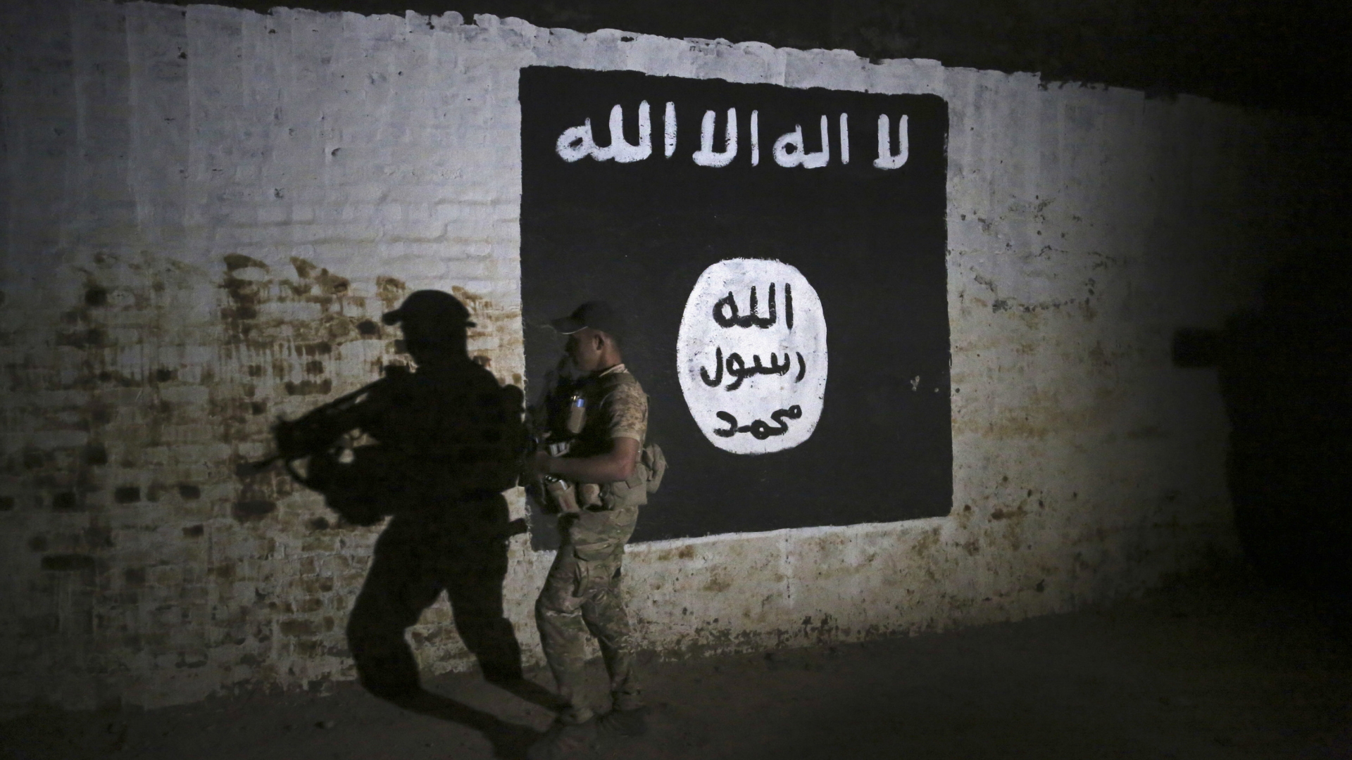 Ein kurdischer Kämpfer geht an einer Wand mit IS-Flagge vorbei.
