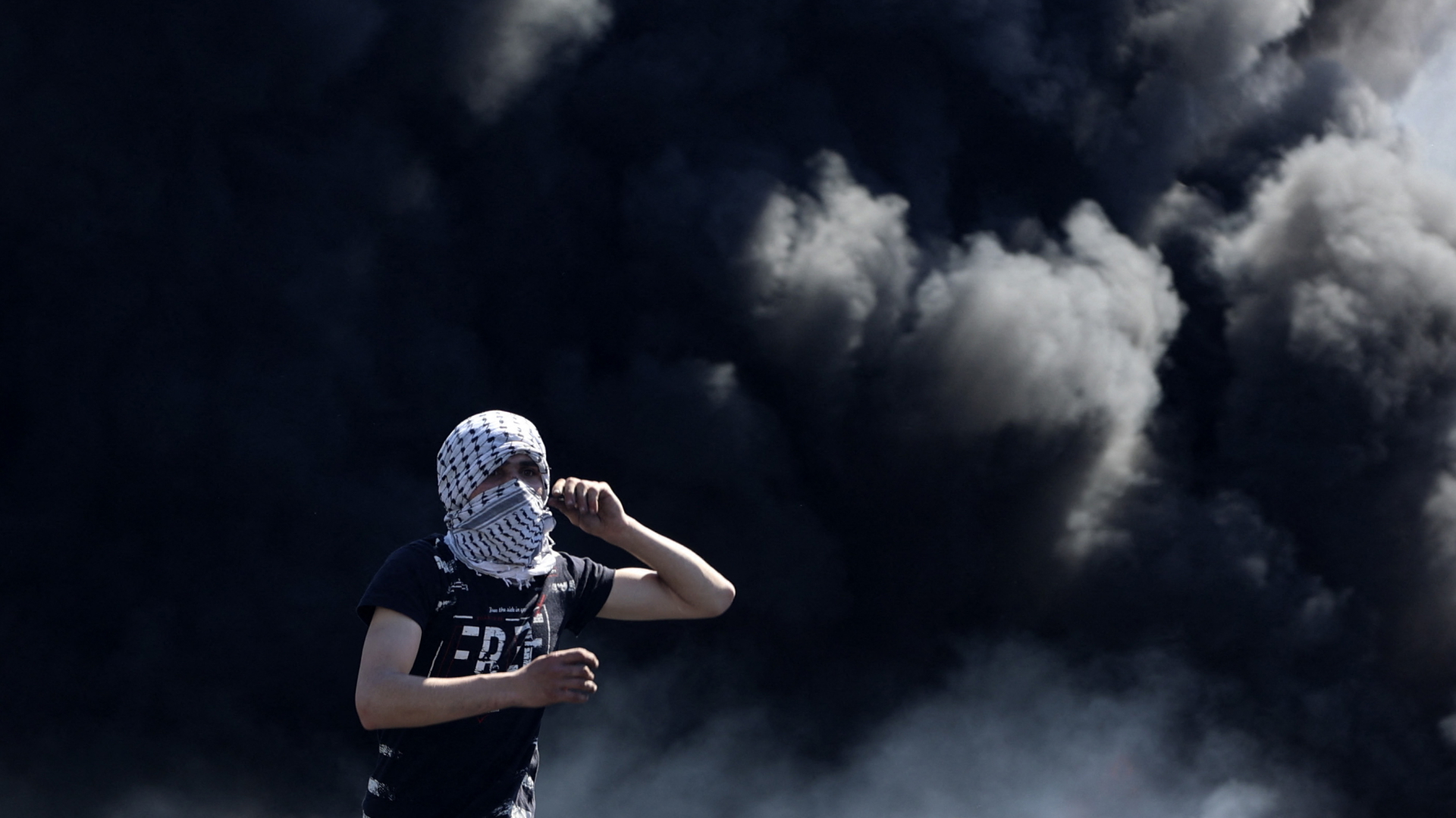 Ein vermummter Palästinenser steht im Gazastreifen vor schwarzen Rauchschwaden.