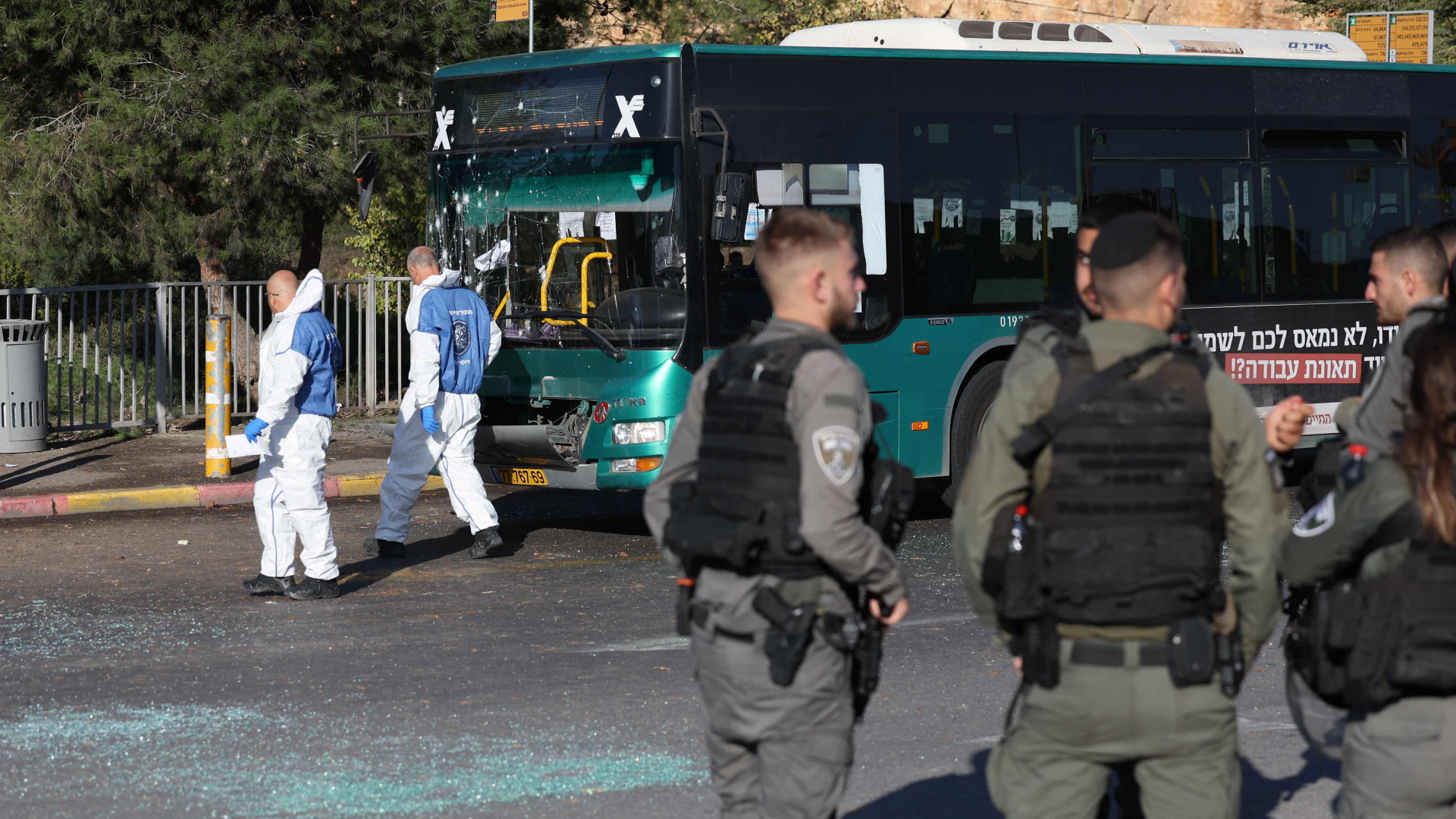 Polizisten und Einsatzkräfte der Spurensicherung sichern nach einem mutmaßlichen Anschlag an einer Bushaltestelle im Großraum Jerusalem den möglichen Tatort mit einem beschädigten Bus. | AFP