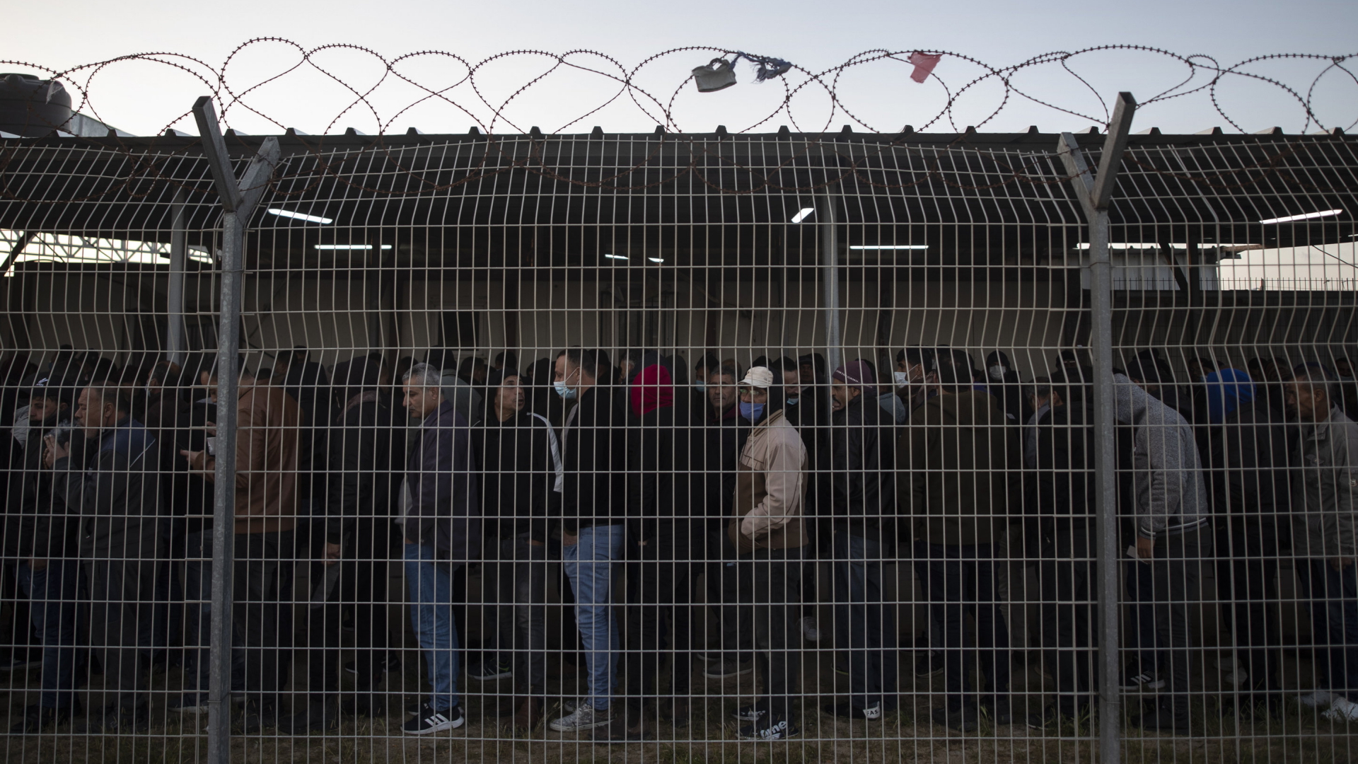 Palästinenser warten hinter einem Stacheldrahtzaun am Grenzübergang Erez, um nach Israel zu gelangen. | AP