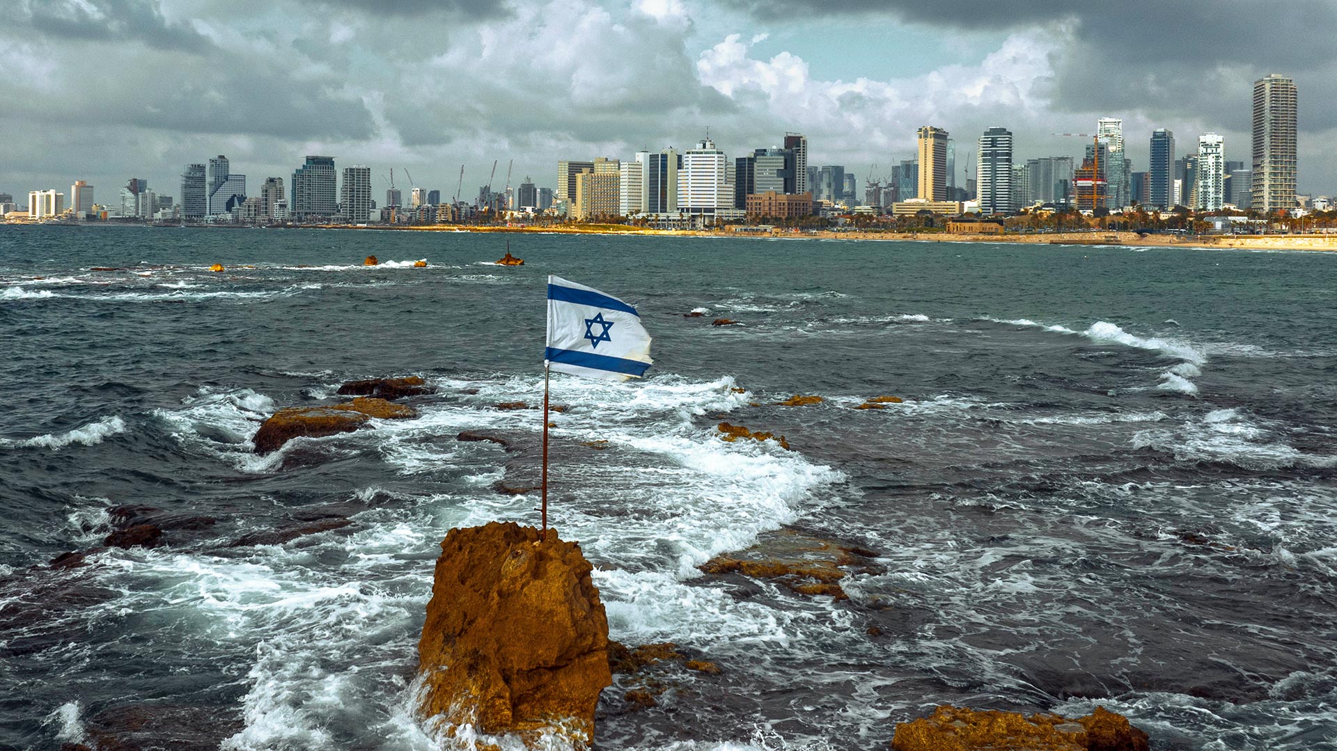 Skyline von Tel Aviv  vom Meer aus gesehen mit einer israelischen Flagge im Vordergrund.
