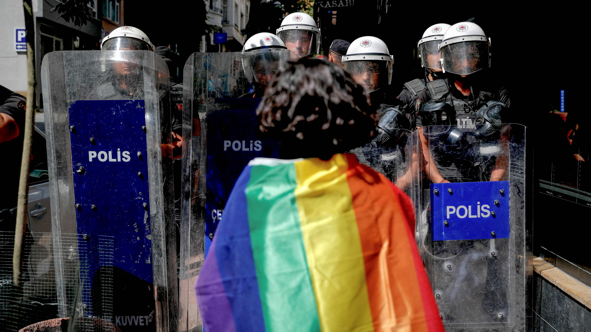Eine Demonstrantin mit Regenbogenflagge steht bei einer Pride-Parade vor mehreren Polizisten. | AFP