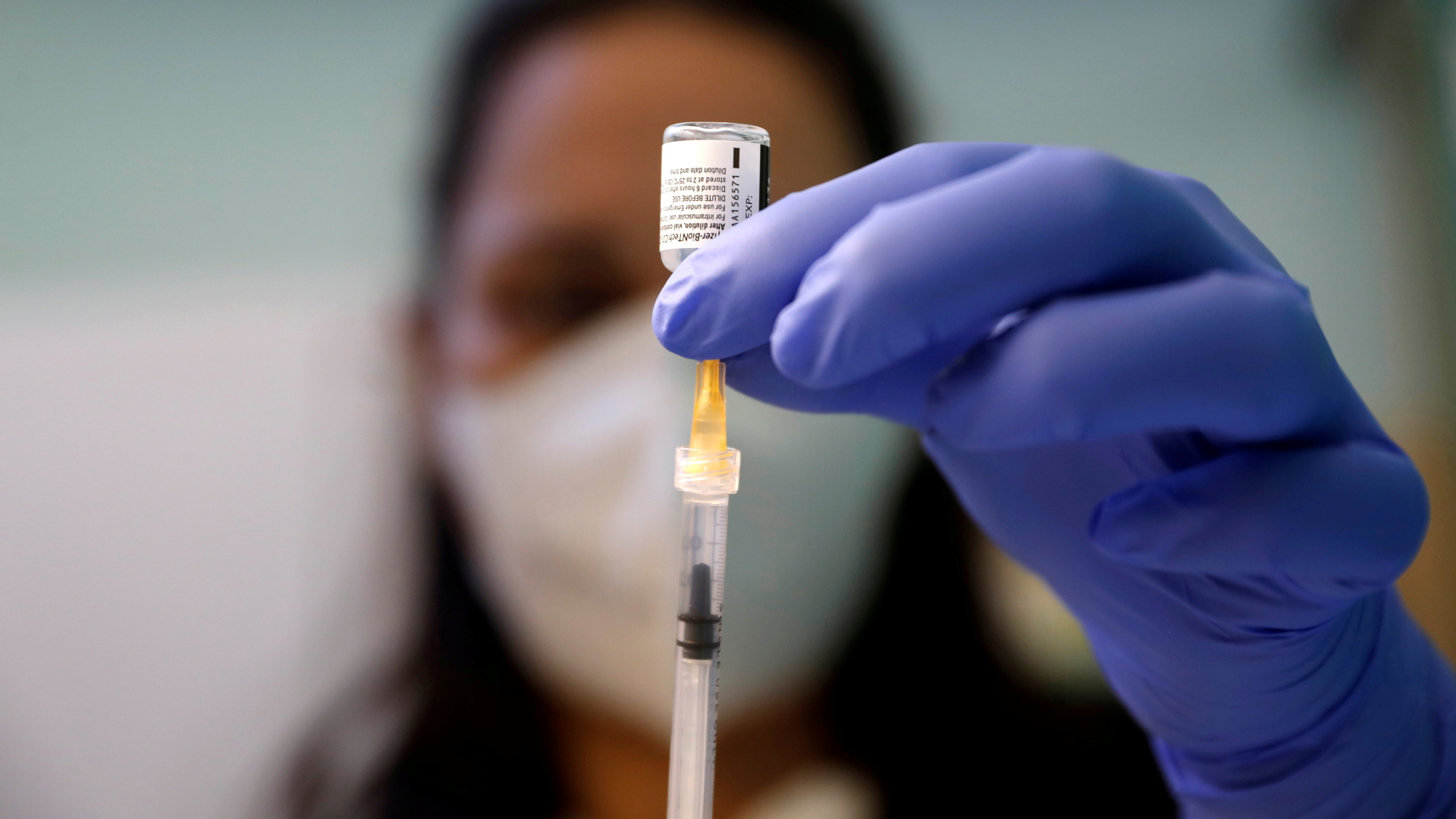 Unscharf ist eine medizinische Mitarbeiterin zu erkennen, die eine Spritze mit dem Corona-Vakzin von BioNTech und Pfizer aufzieht. | REUTERS