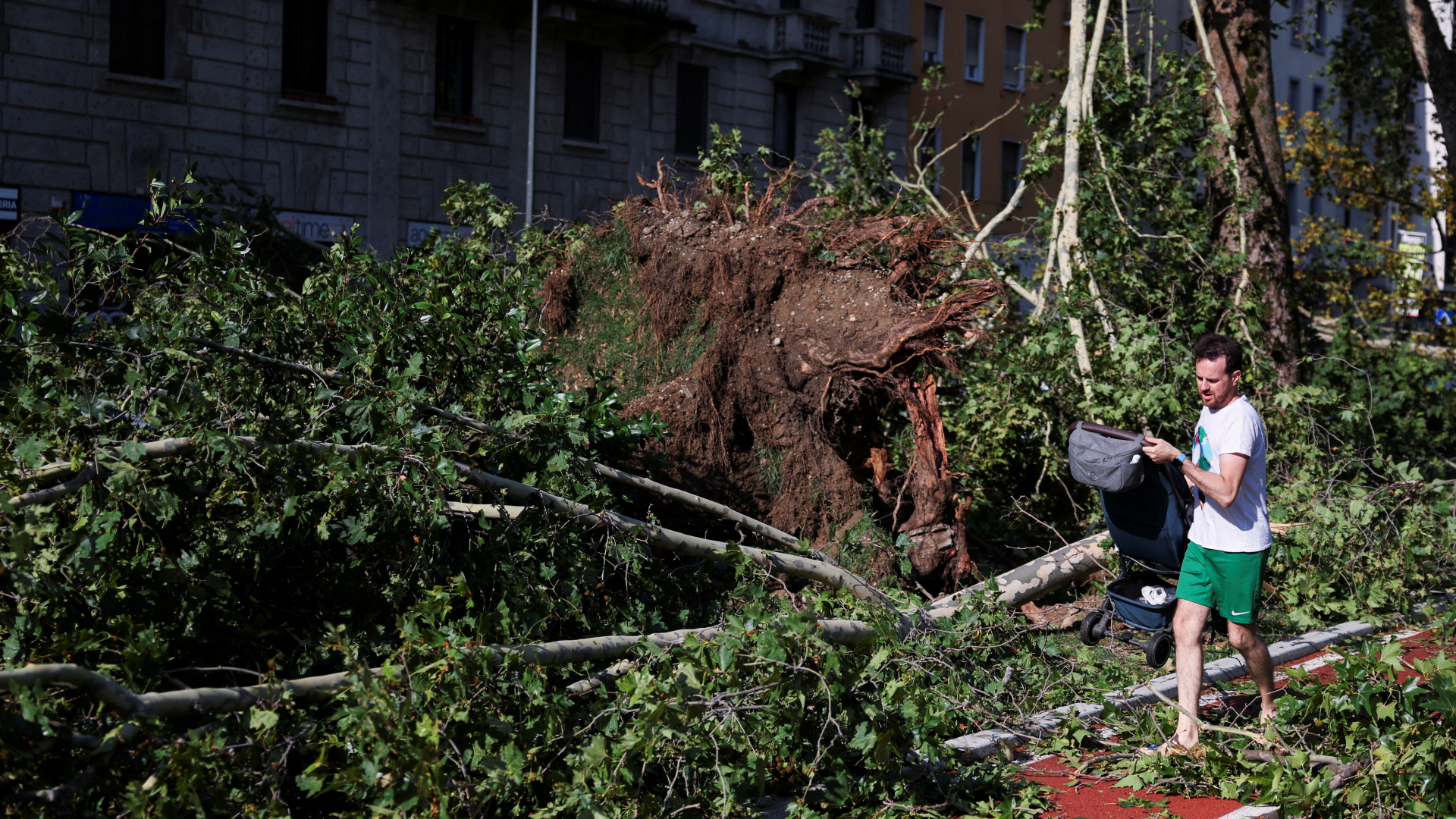 Ein Mann läuft in Mailand mit einer Tasche im Arm an umgestürzten Bäumen vorbei.
