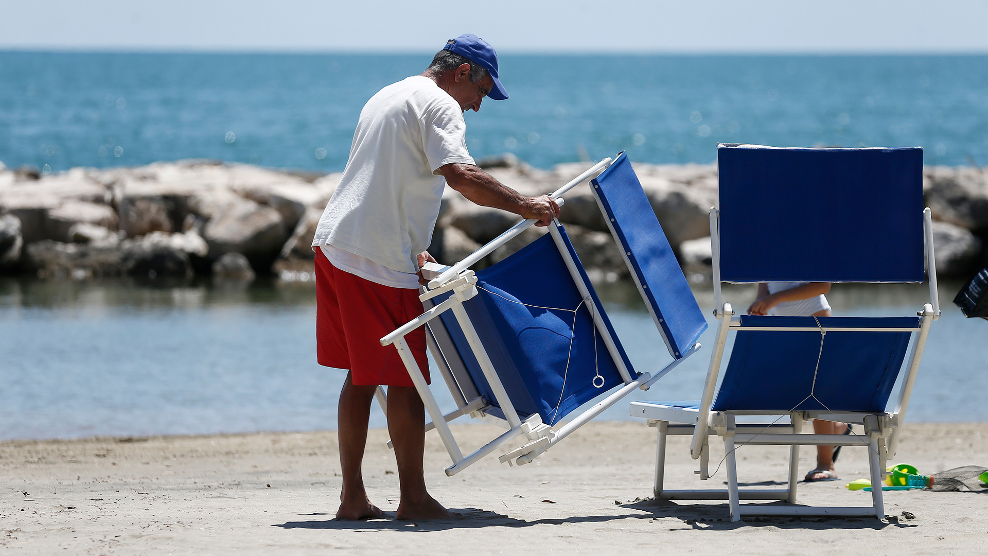 Ein Hotelmitarbeiter stellt Liegestühle am Golf von Gaeta auf (Archuivbild).  | dpa