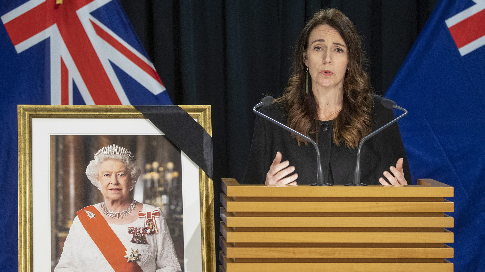 Jacinda Ardern spricht neben einem Bild von Queen Elizabeth II. | AP
