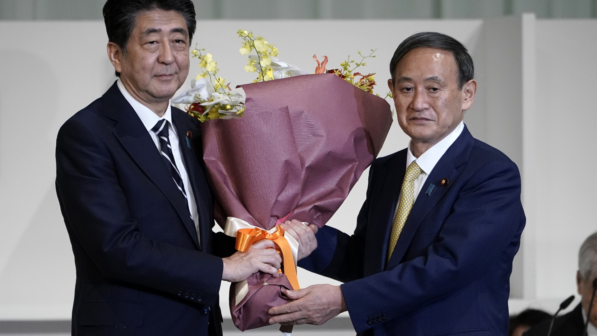 Japans Premierminister Shinzo Abe und sein designierter Nachfolger Yoshihide Suga halten ein Blumenbouquet. | AP