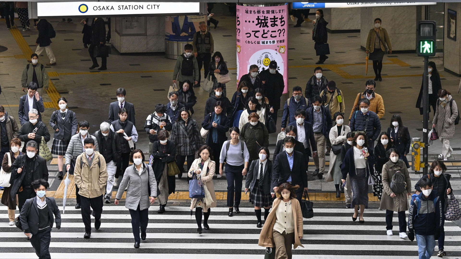 Menschen mit Masken und ohne Masken gehen im japanischen Osaka über eine Straße. | dpa