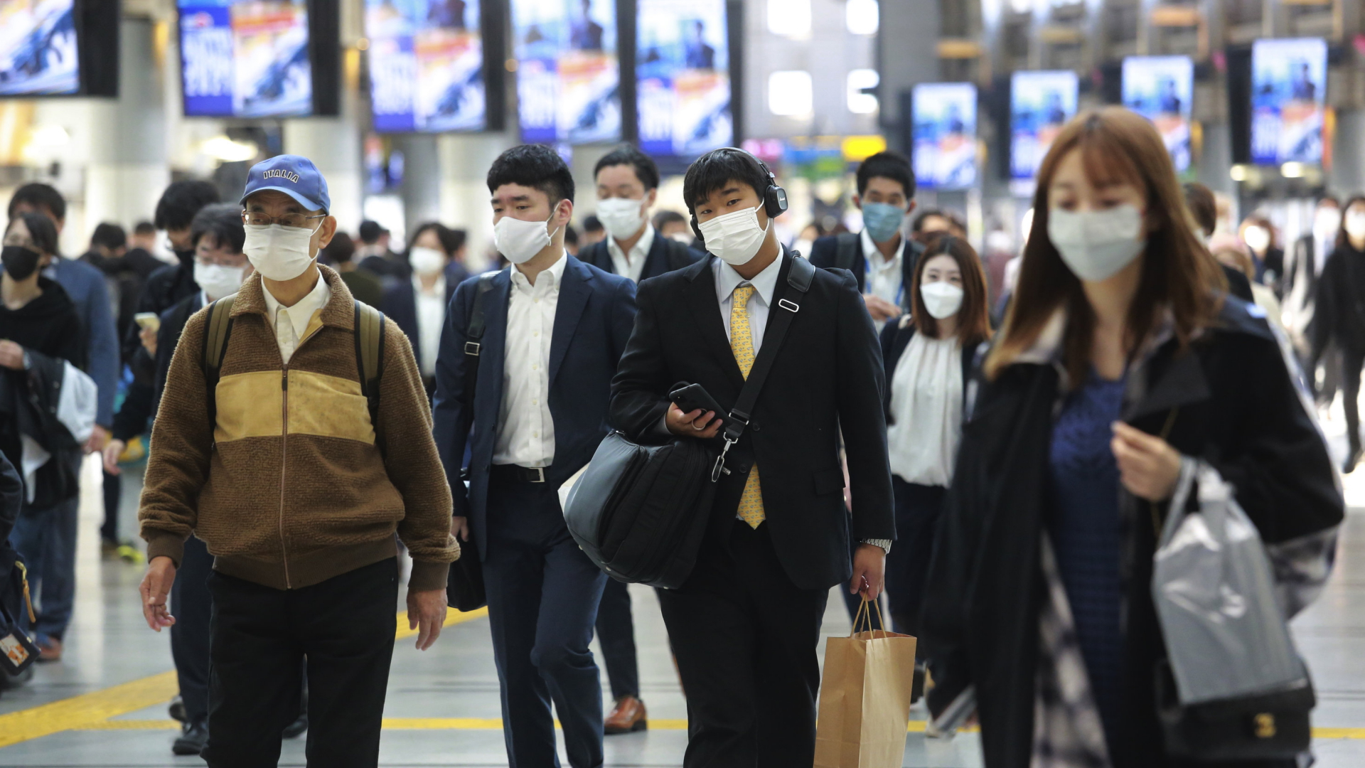 Menschen mit Mund-Nasen-Masken laufen durch eine Bahnstation in Tokio. | AP