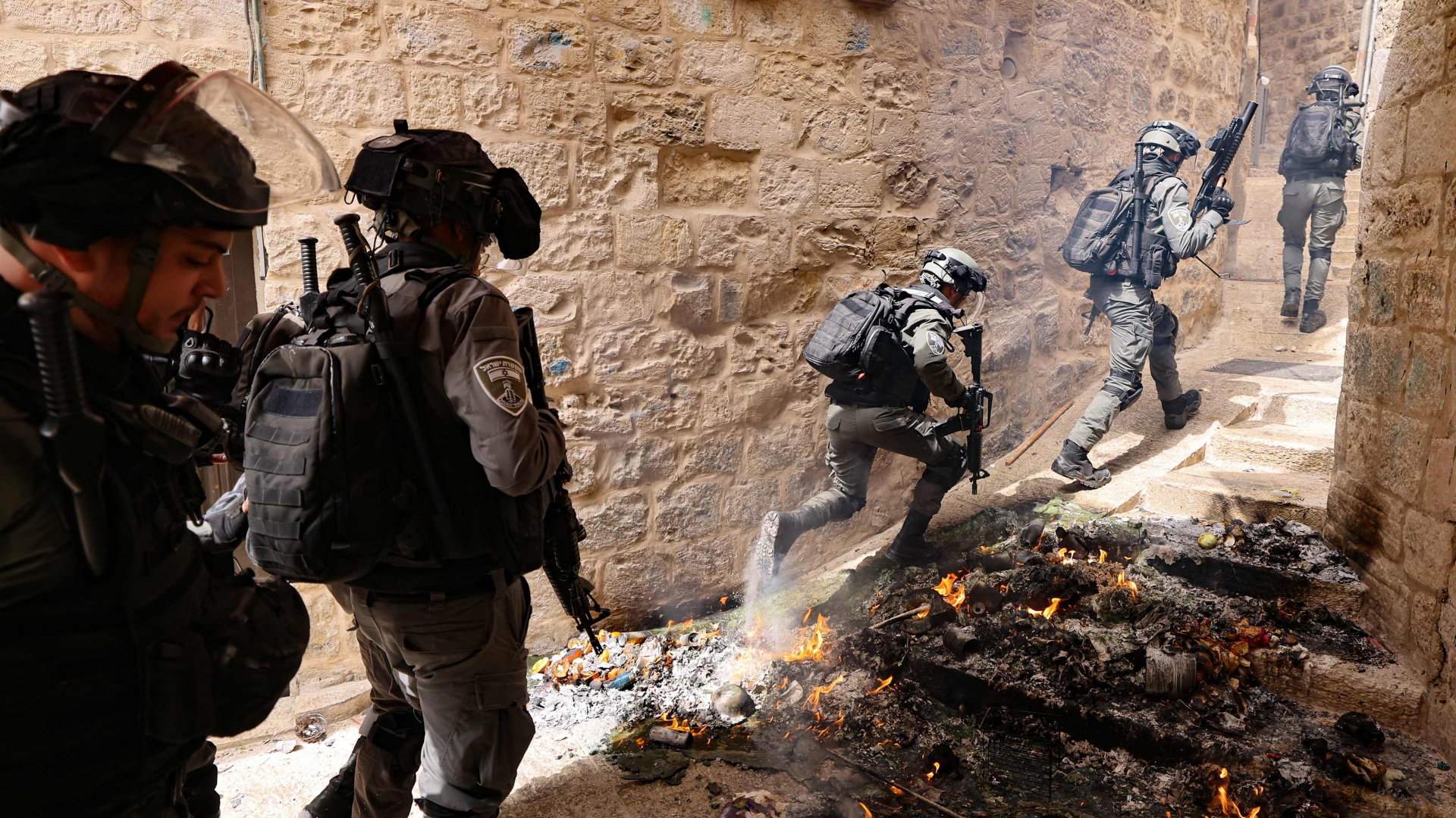 Bewaffnete israelische Sicherheitskräfte laufen während Ausschreitungen in der Altstadt von Jerusalem durch die Reste einer brennenden Barrikade. | AFP