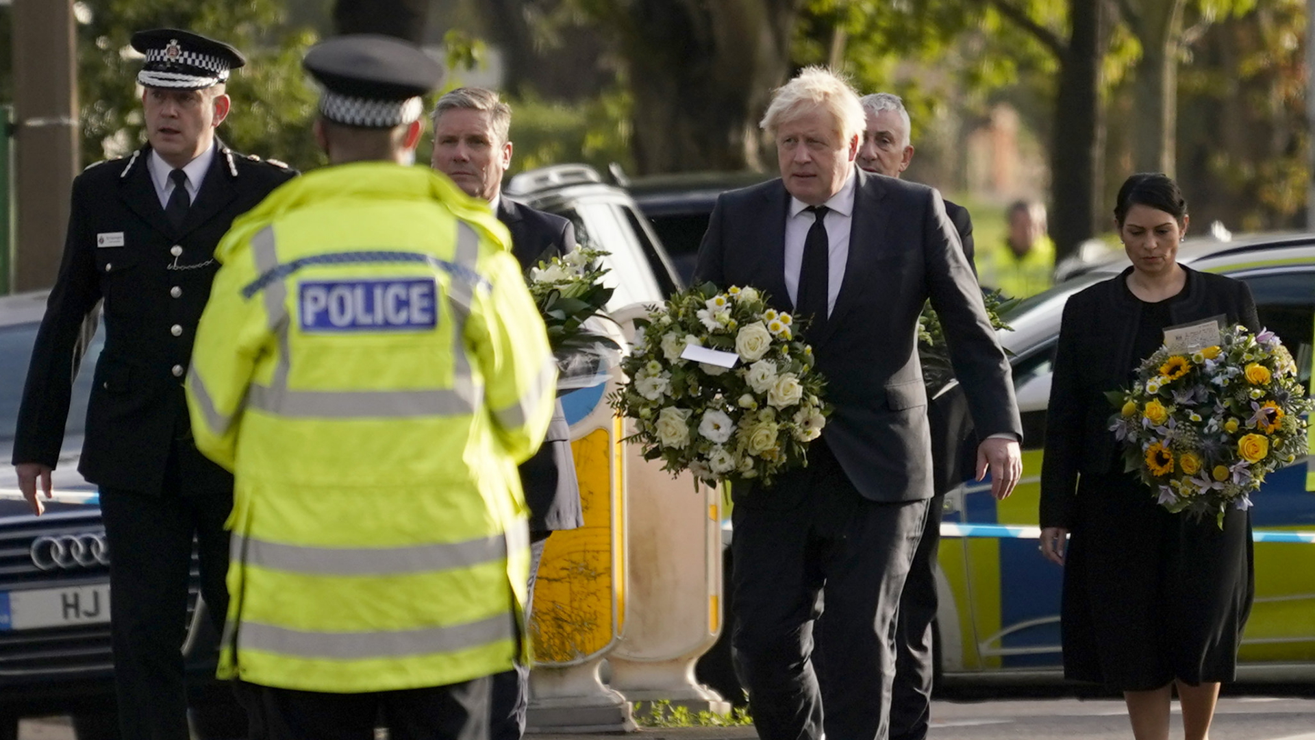 Der britische Premierminister Boris Johnson trägt Blumen zum Ort des Attentats auf den Abgeordneten David Amess, bewacht von einem Polizisten. | AP