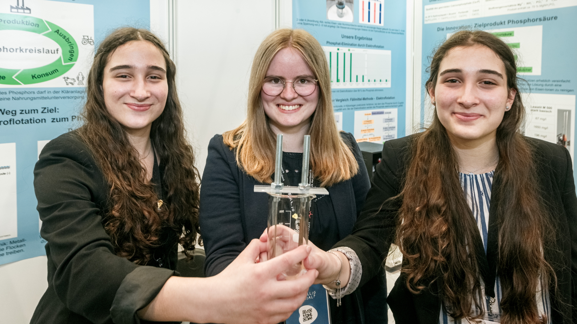 Die Chemie-Bundessiegerinnen Lena Fries (von li. nach re.), Hannah Amrhein und Hanna Fries, halten ihr Forschungswerkzeug, ein Becherglas mit Elektroden. | dpa