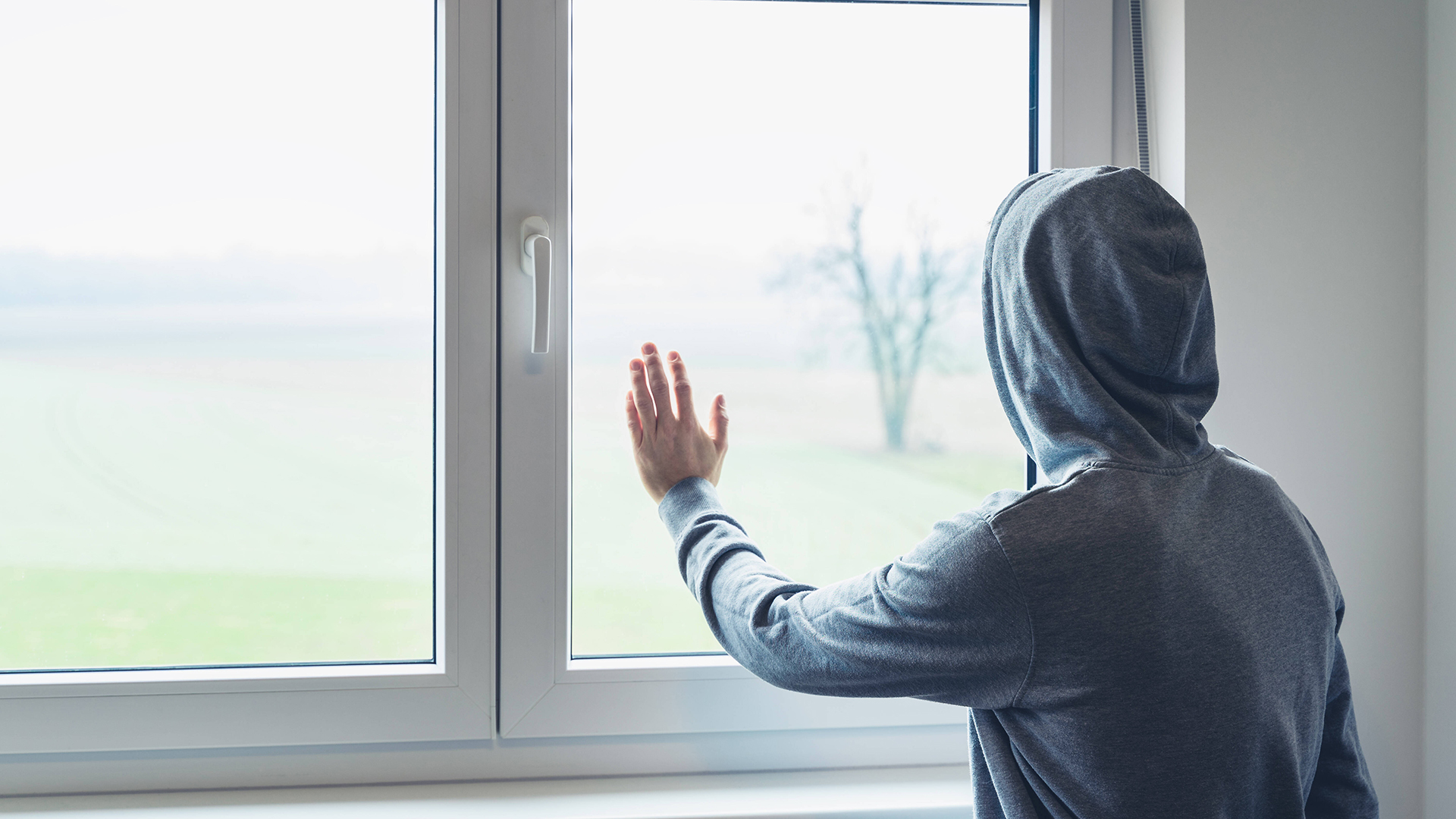 Ein Jugendlicher schaut aus dem Fenster. | imago images/Bihlmayerfotografie