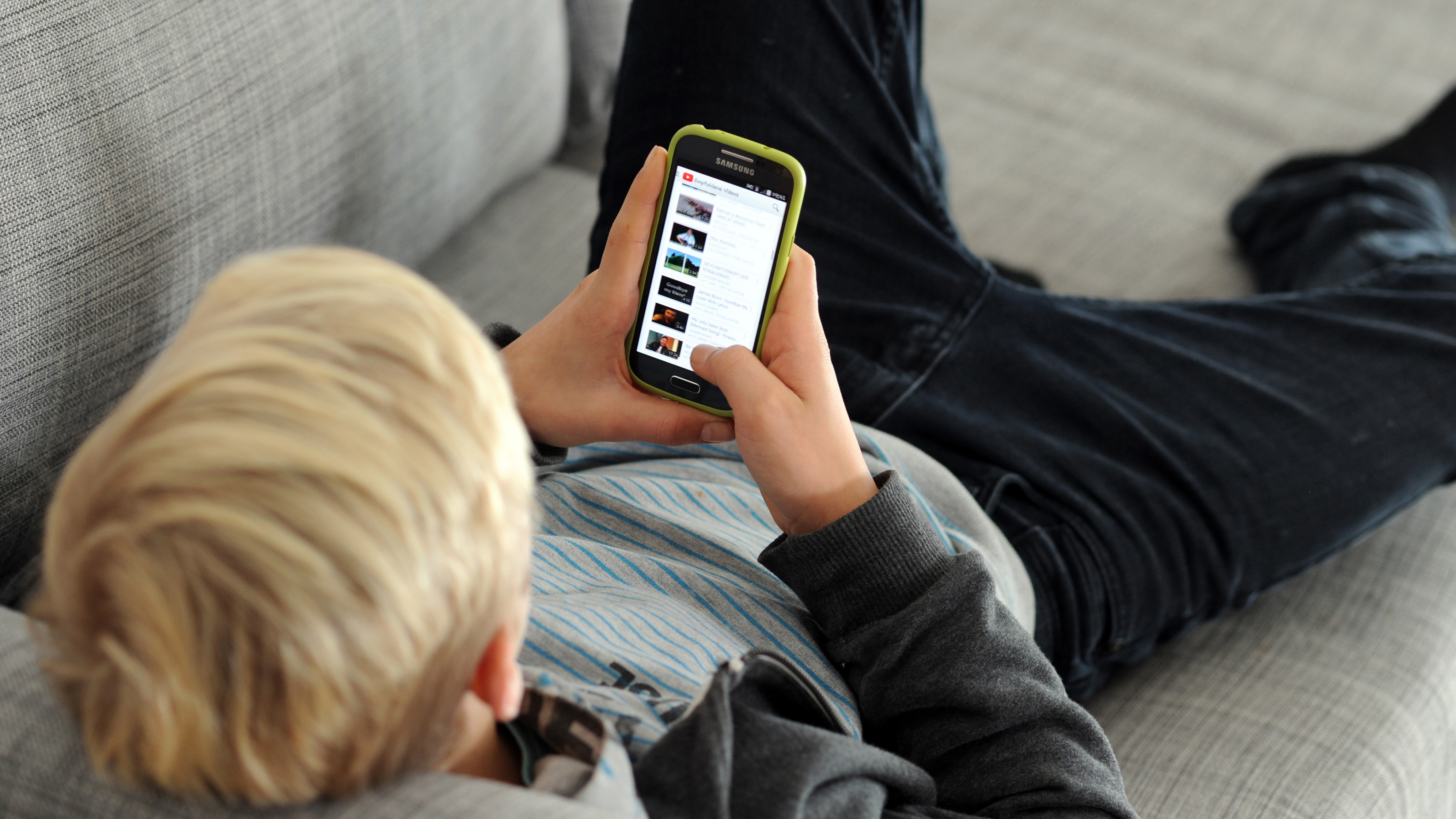 Ein Junge liegt auf einem Sofa und guckt auf ein Smartphone. | picture alliance / Tobias Hase/d