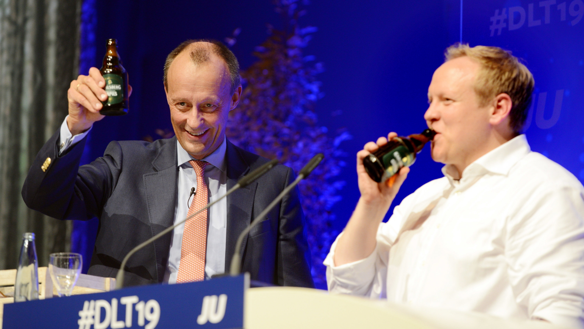Friedrich Merz (l, CDU), Vizepräsident des Wirtschaftsrats, und Tilman Kuban, Bundesvorsitzender der Jungen Union Deutschland, trinken nach der Rede von Merz beim Deutschlandtag der Jungen Union auf der Bühne zusammen Bier.  | dpa