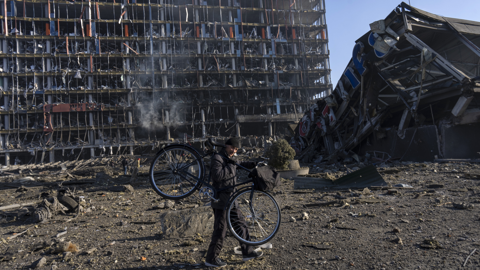 Ein Mann trägt sein Fahrrad an einem durch Bombardierung zerstörten Einkaufszentrum in Kiew vorbei. | dpa