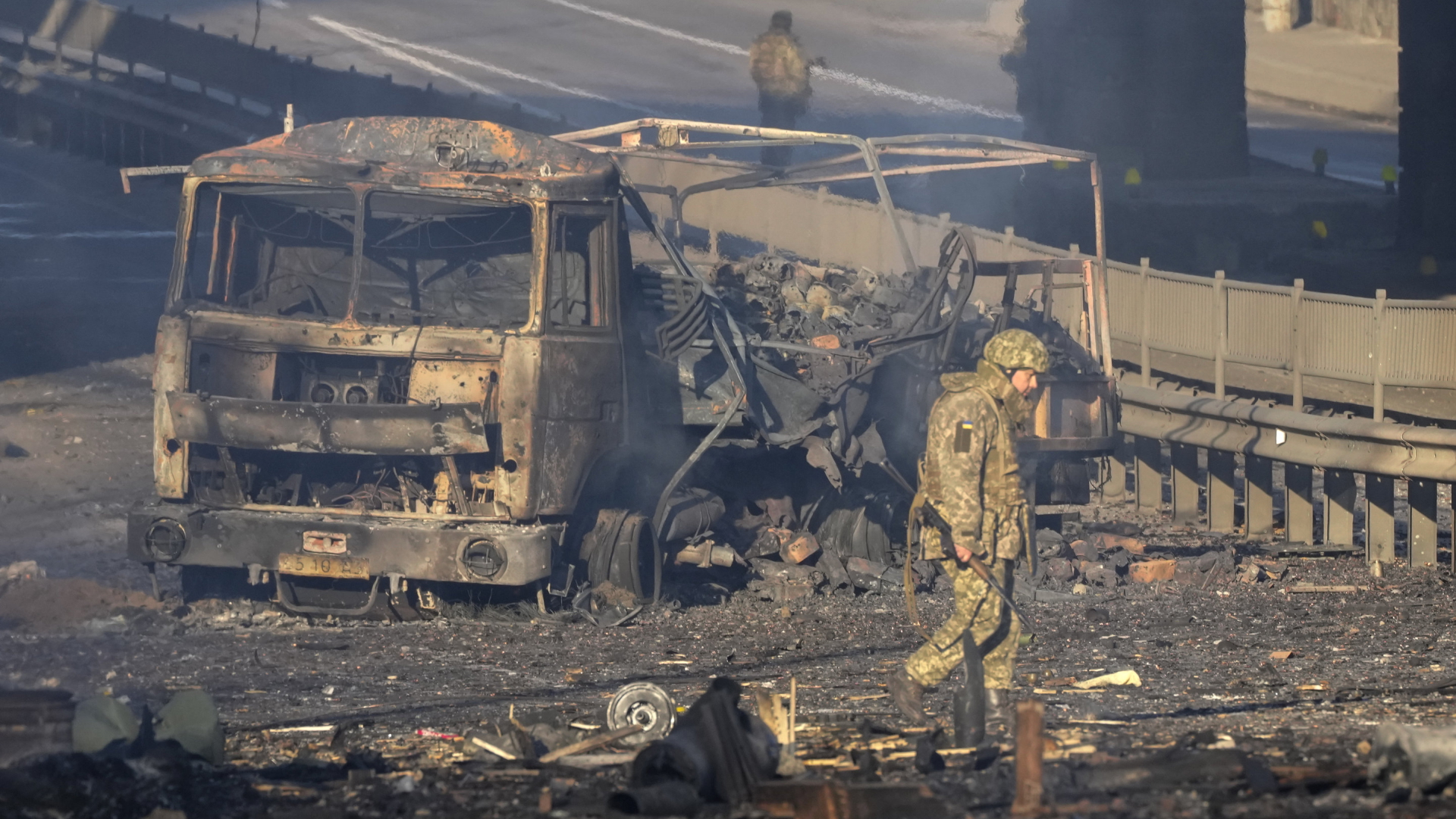 Ein ukrainischer Soldat geht in Kiew an einem zerstörten Fahrzeug vorbei | AP