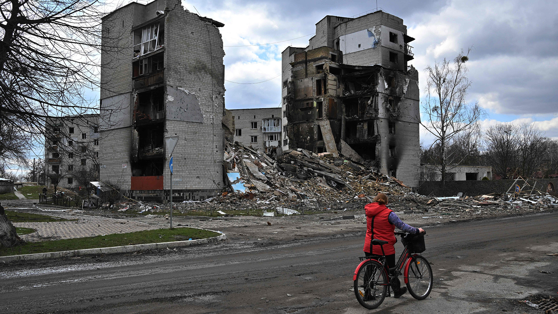 Eine Frau schiebt ein Fahrrad an zerstörten Häusern in Kiew vorbei. | AFP