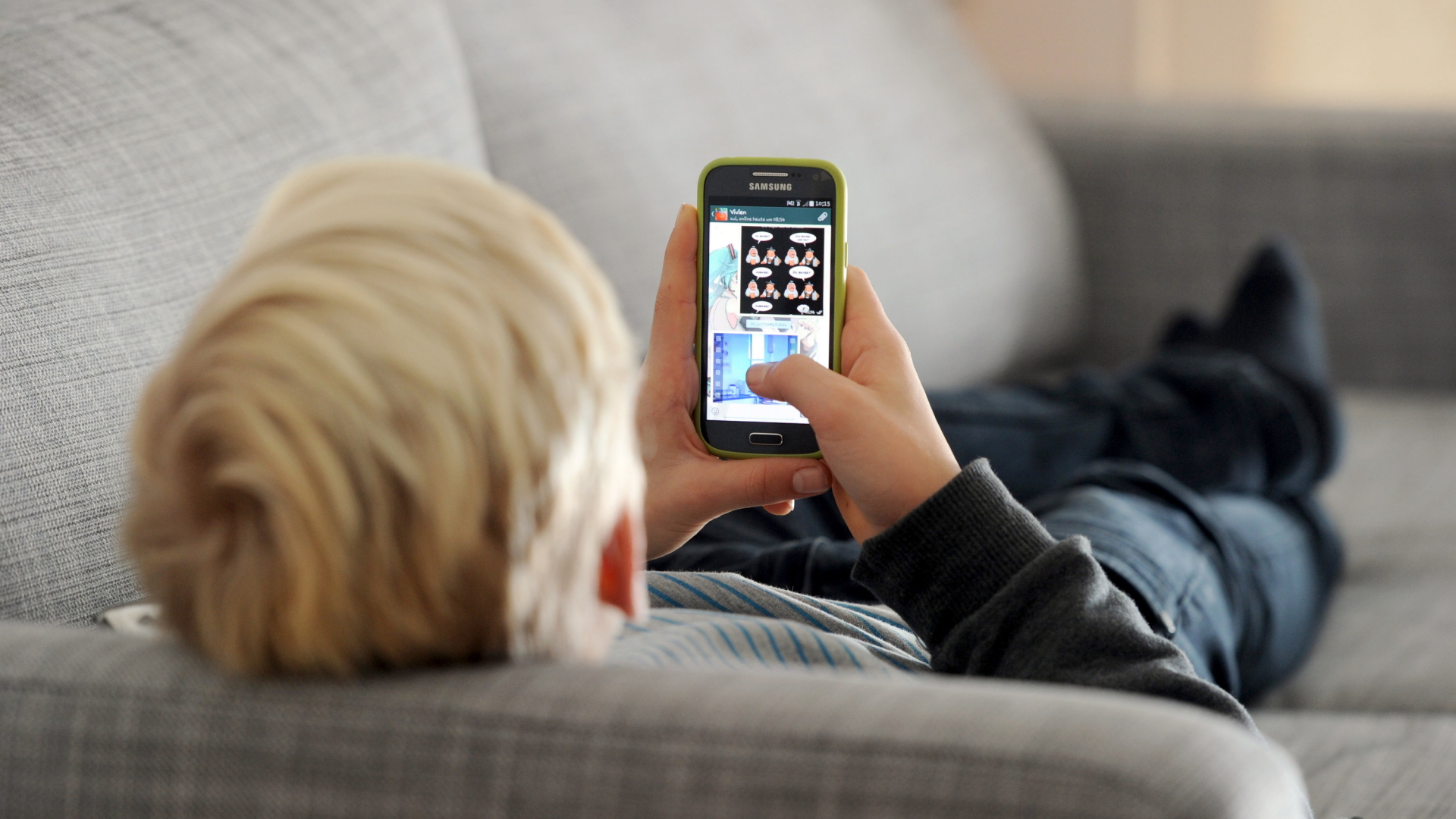 Ein Kind liegt mit einem Smartphone auf dem Sofa. | dpa