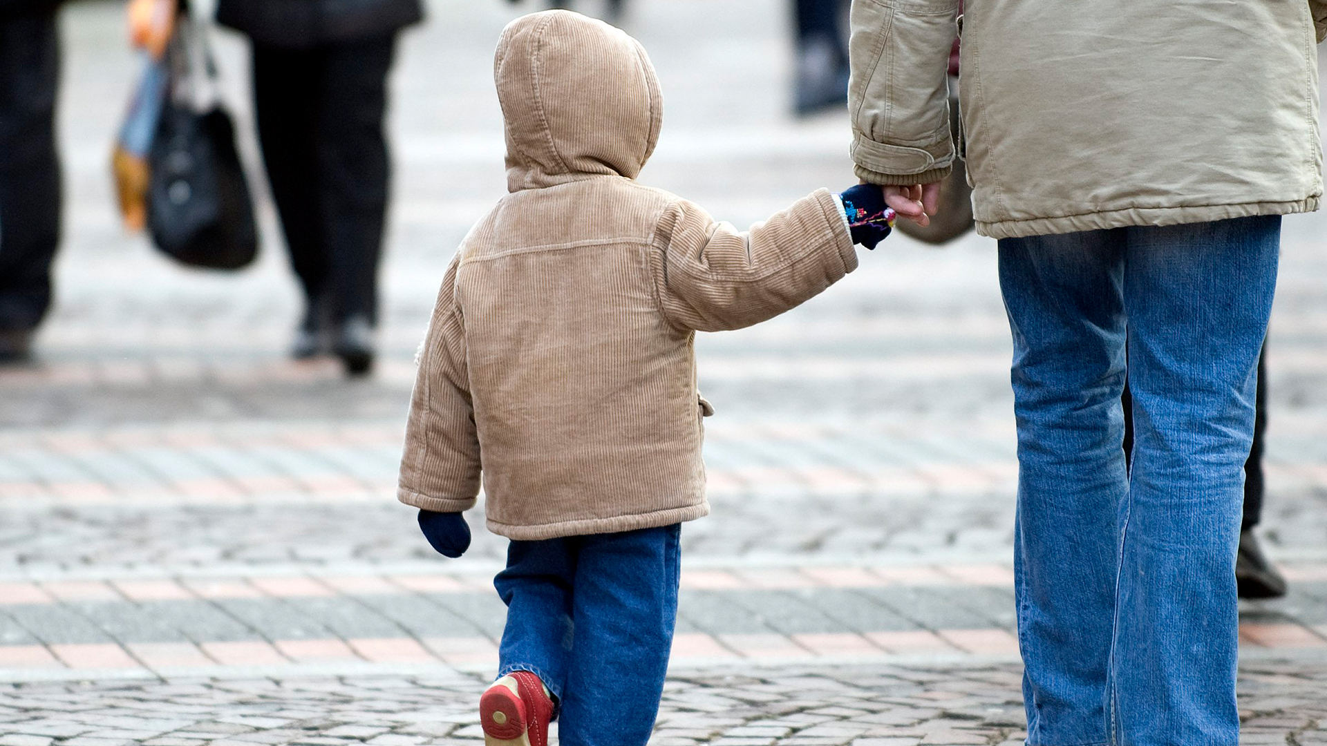 Ein kleines Kind geht an der Hand eines Erwachsenen eine Straße entlang. | AP