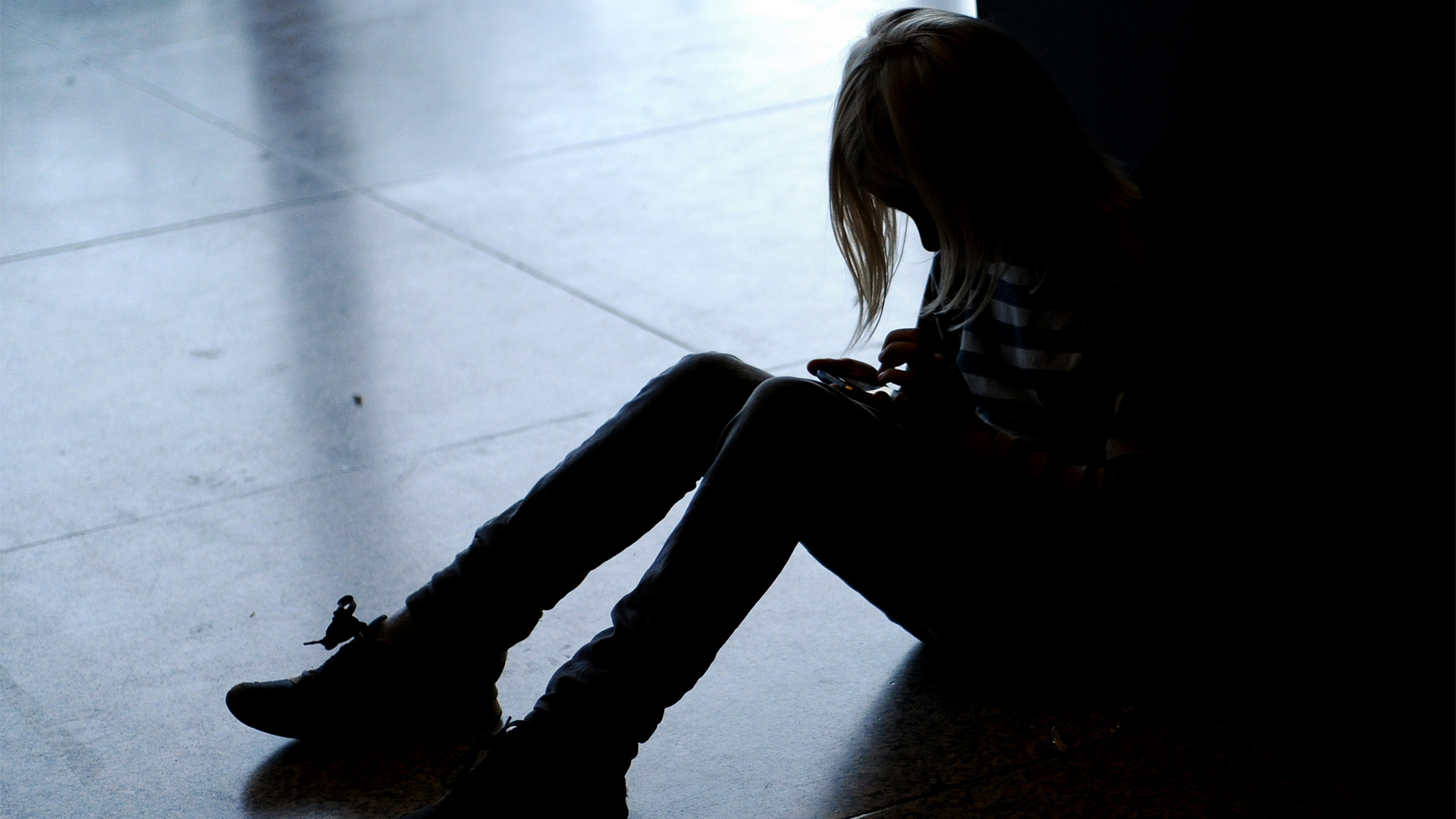Ein Mädchen sitzt mit gesenktem Kopf allein auf dem Fußboden. 