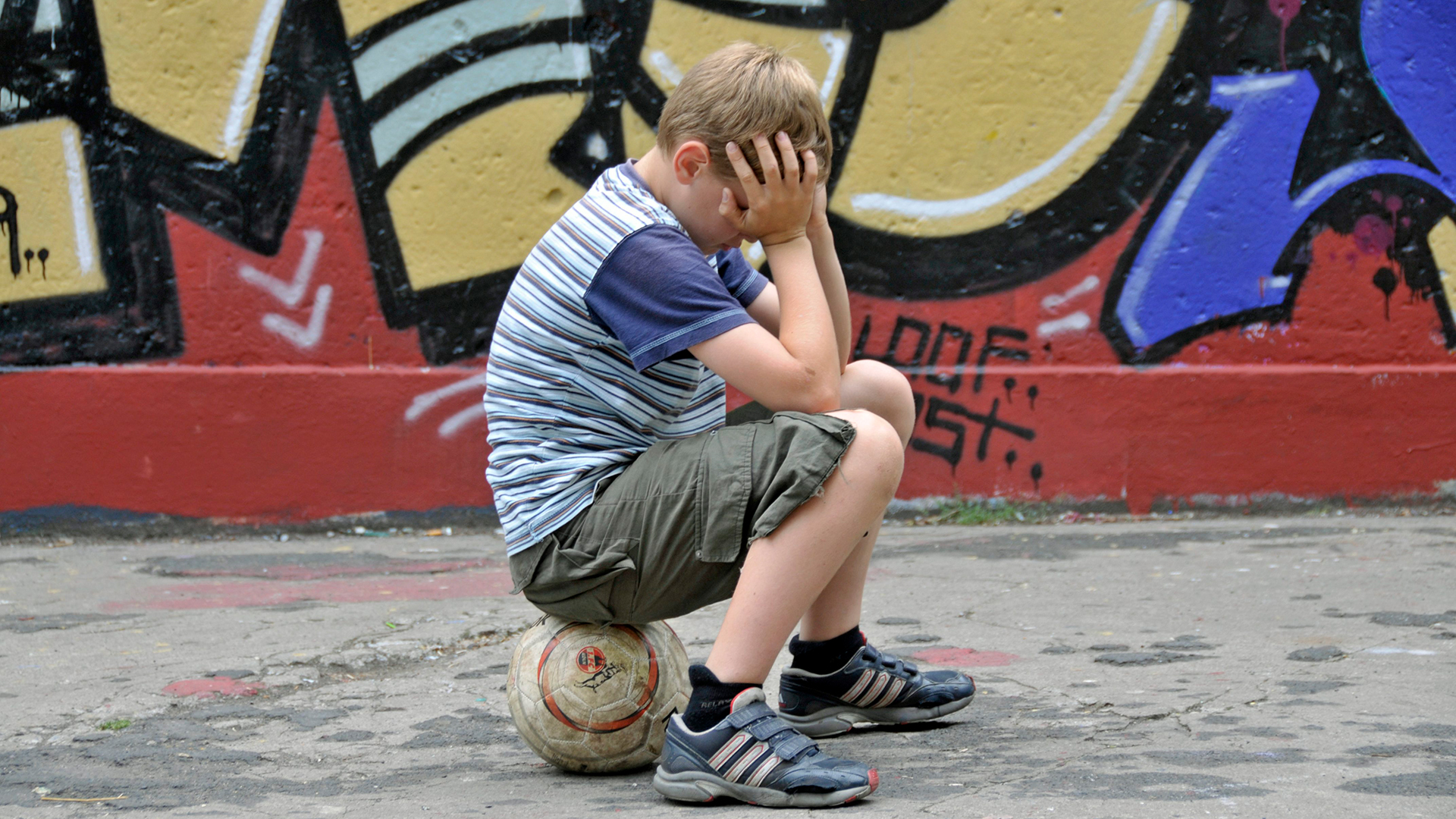 Ein Junge sitzt auf einem Ball und hält sich die Hände vor das Gesicht | Alliance