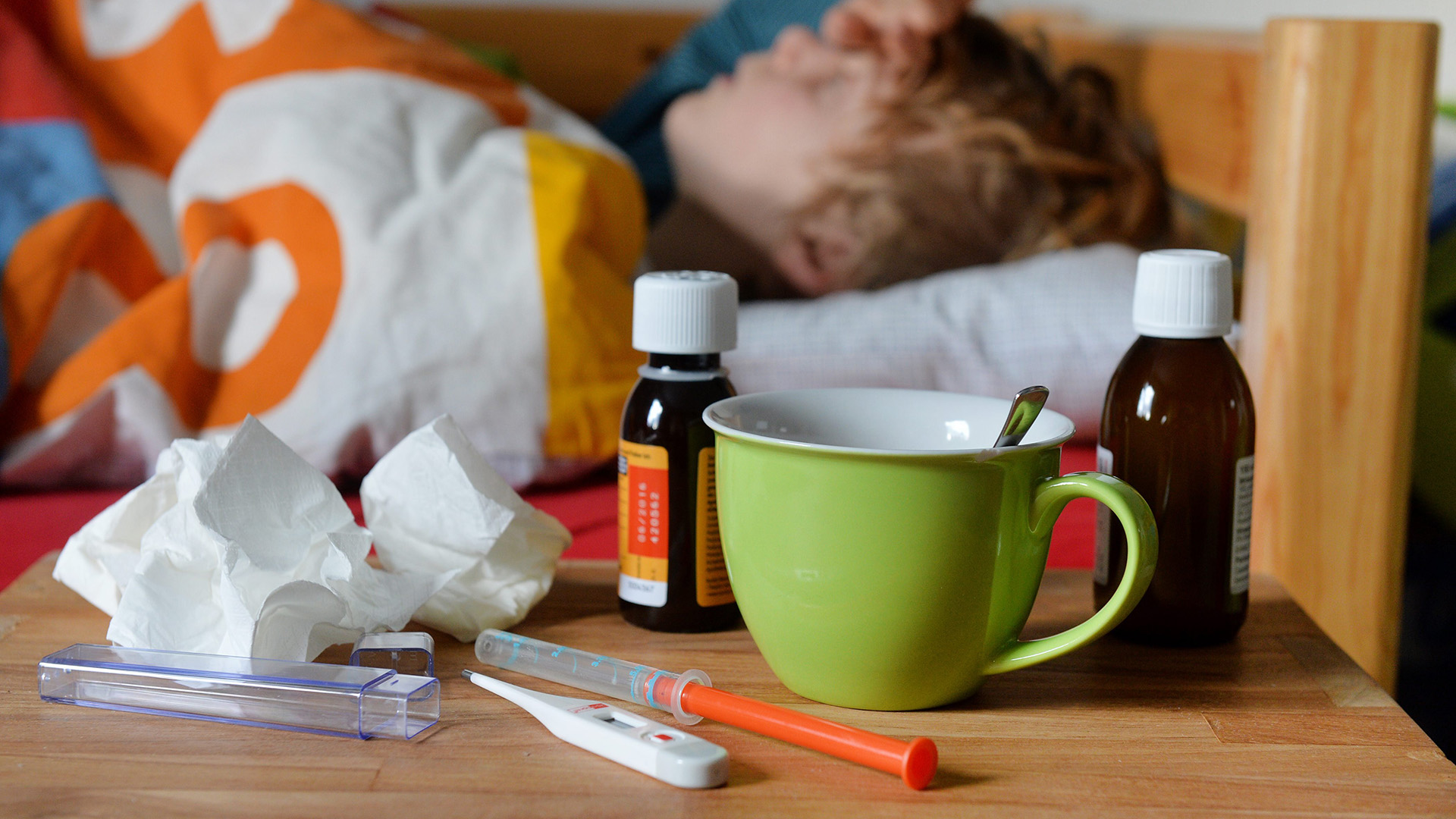 Fiebersaft, Fieberthermometer, Taschentücher und eine Tasse am Bett eines Kindes | picture alliance / Frank May