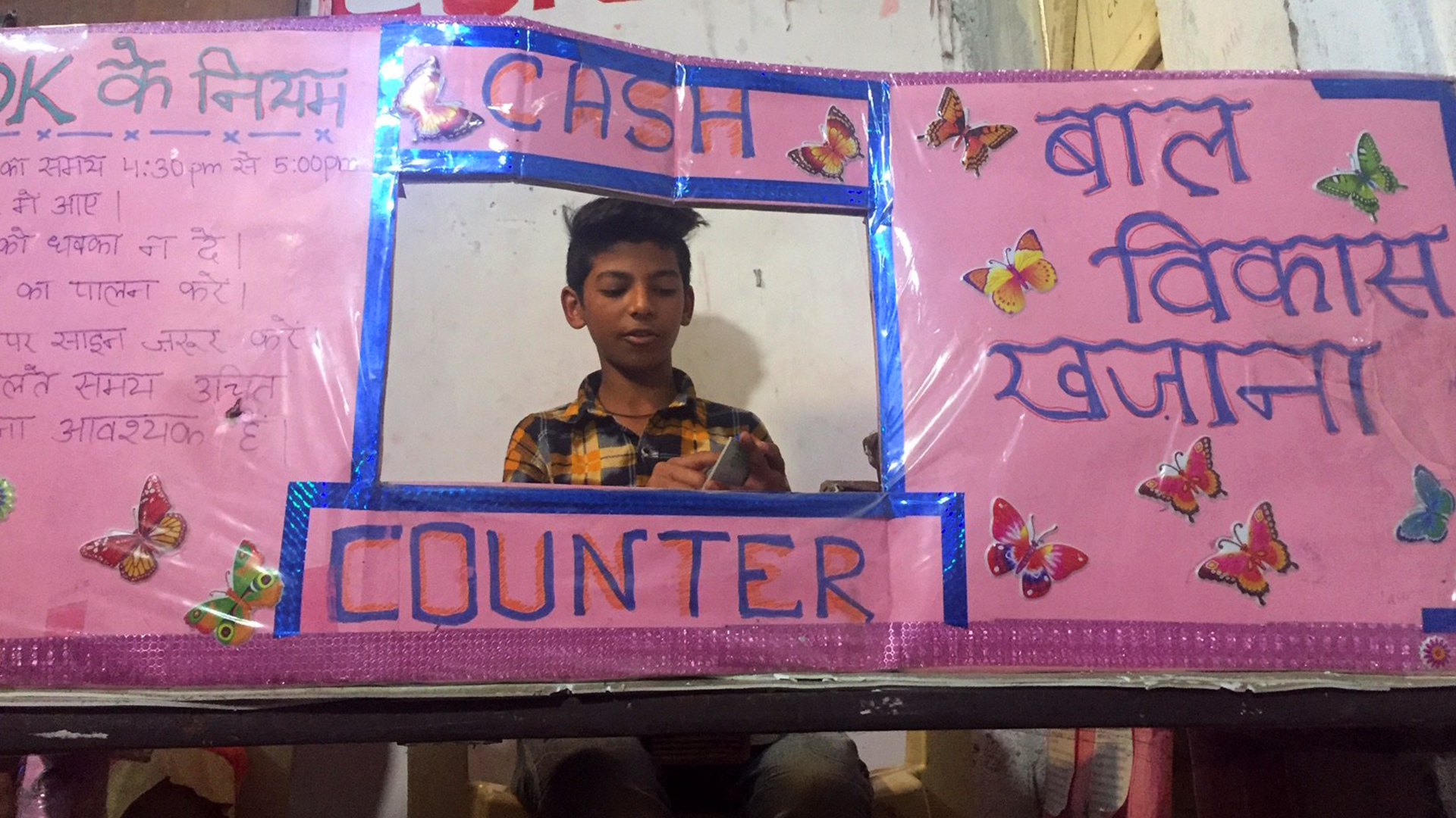 Sheikh Sameer ist gut in Mathe und wurde daher zum Bankmanager gewählt. Hier sitzt er hinter "seinem" Schalter aus Pappe. | Bildquelle: ARD Neu-Delhi