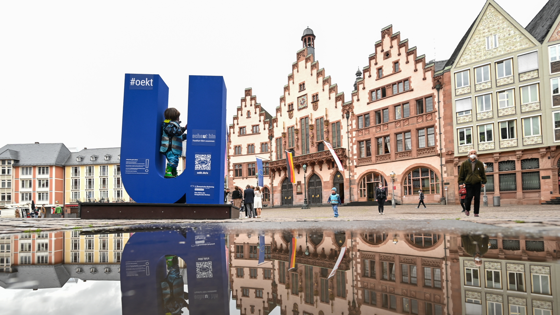 Der Buchstabe "U" aus dem Slogan "schaut hin" für den 3. Ökumenischen Kirchentag spiegelt sich vor dem Fankfurter Rathaus Römer in einer Pfütze. | dpa