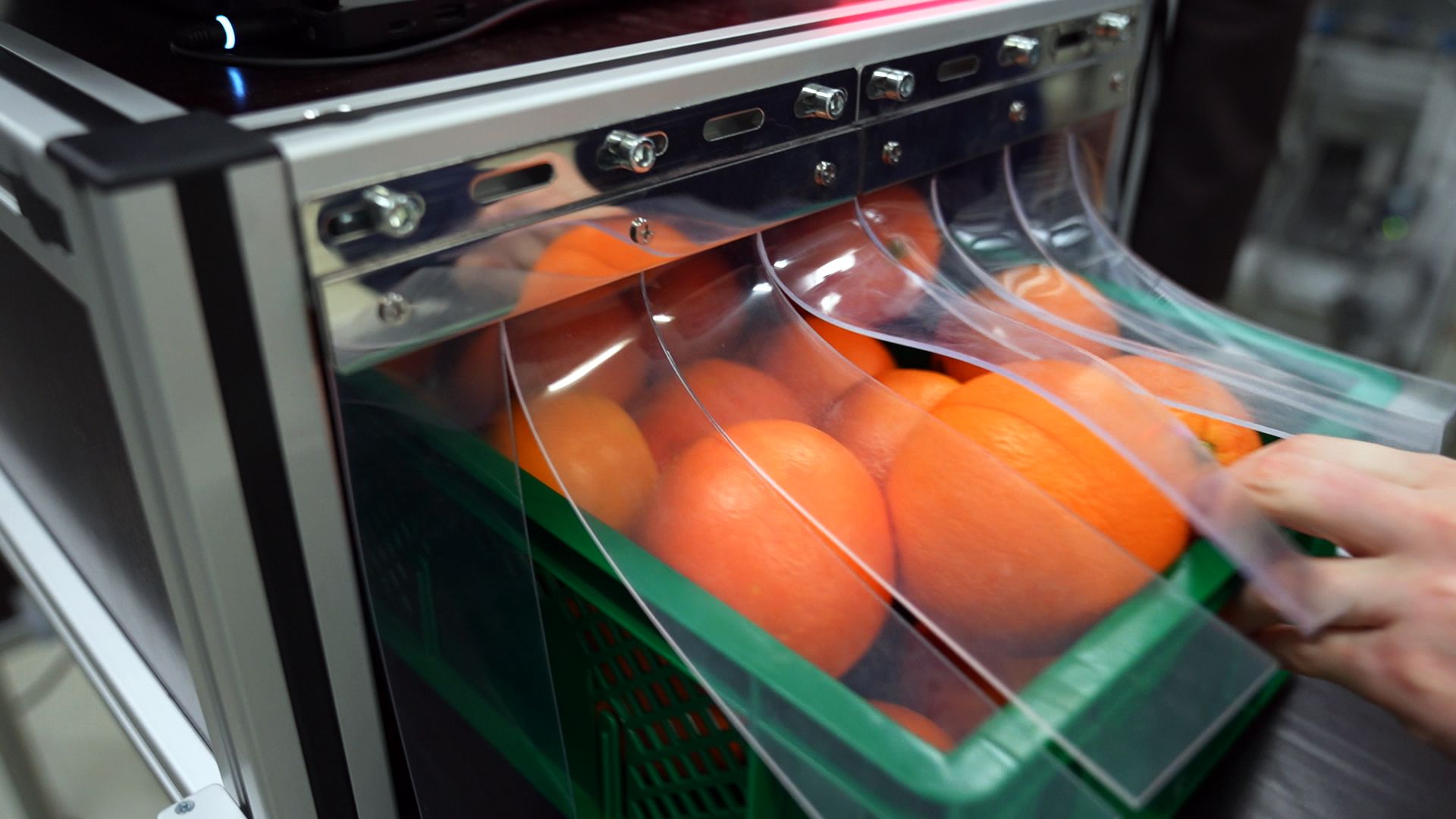 Eine Plastikkiste voller Orangen wird durch eine Maschine geschoben.