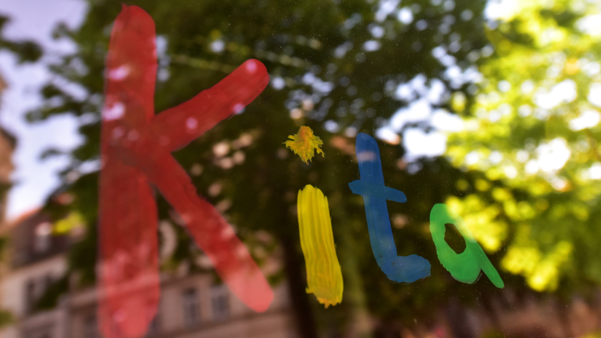 Der bunte Schriftzug "Kita" ist in München mit Fingerfarbe auf die Fensterscheibe einer Kindertagesstätte gemalt (Archivbild) | dpa